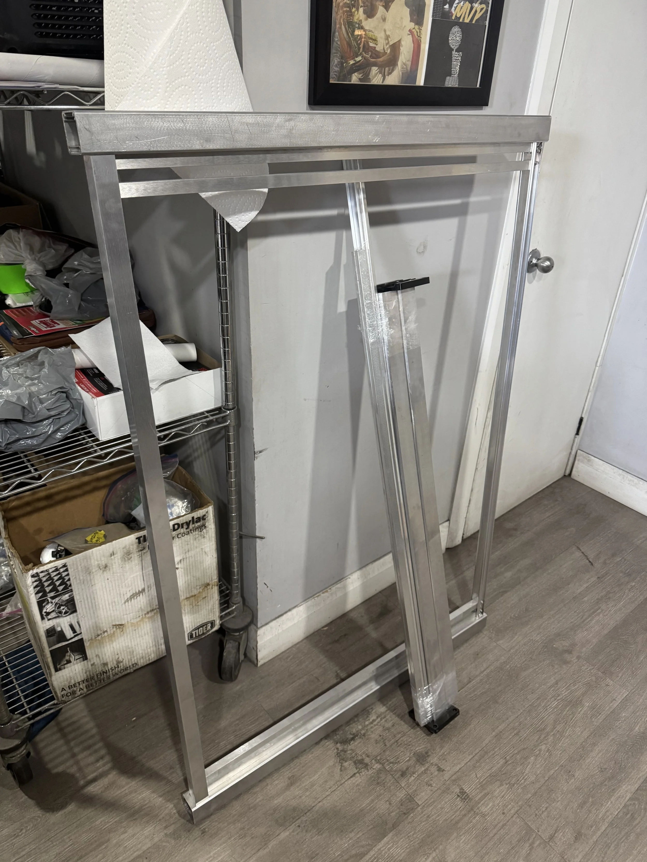 Empty aluminum or metal folding table frame with legs, leaning against a wall in a cluttered room.