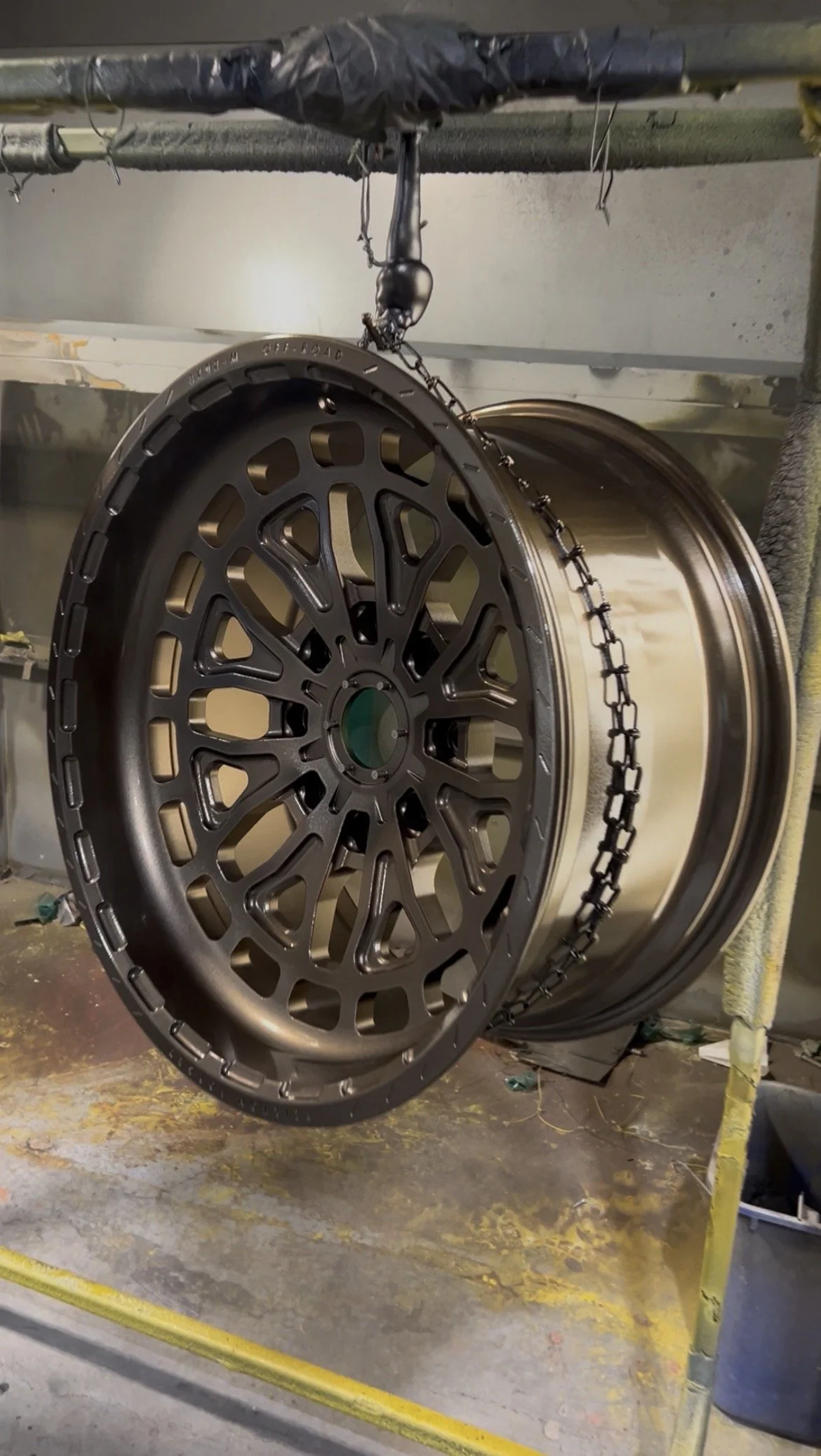 Black alloy wheels hanging from a chain hoist in a workshop, with one wheel in front and the other behind.