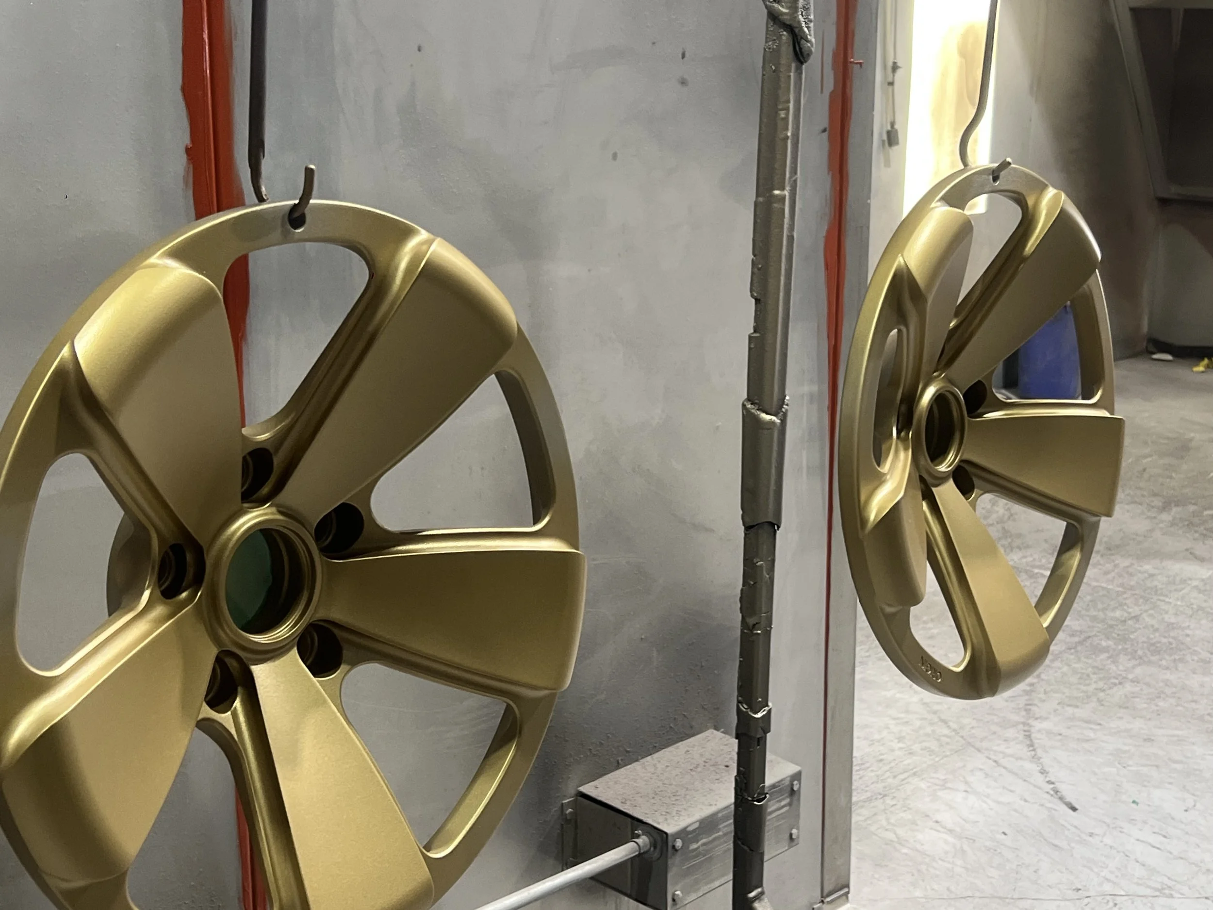 Two gold-colored car wheel rims mounted on a wall in an industrial setting.