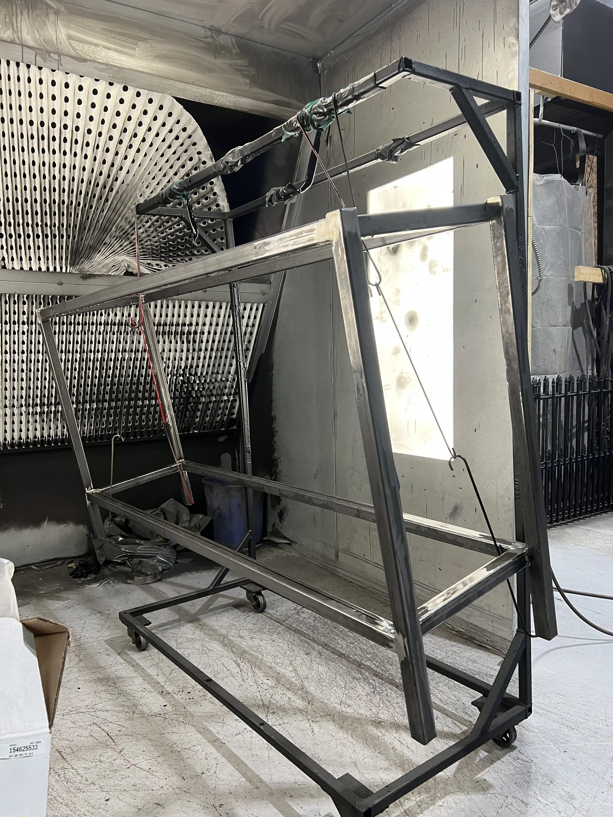 Metal framework structure on wheels in a workshop, with tools and materials around, and industrial vents or ducts in the background.