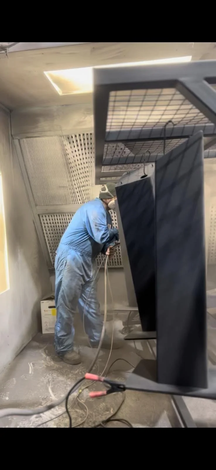 A person in protective gear working inside a confined space with electronic equipment and wires visible.