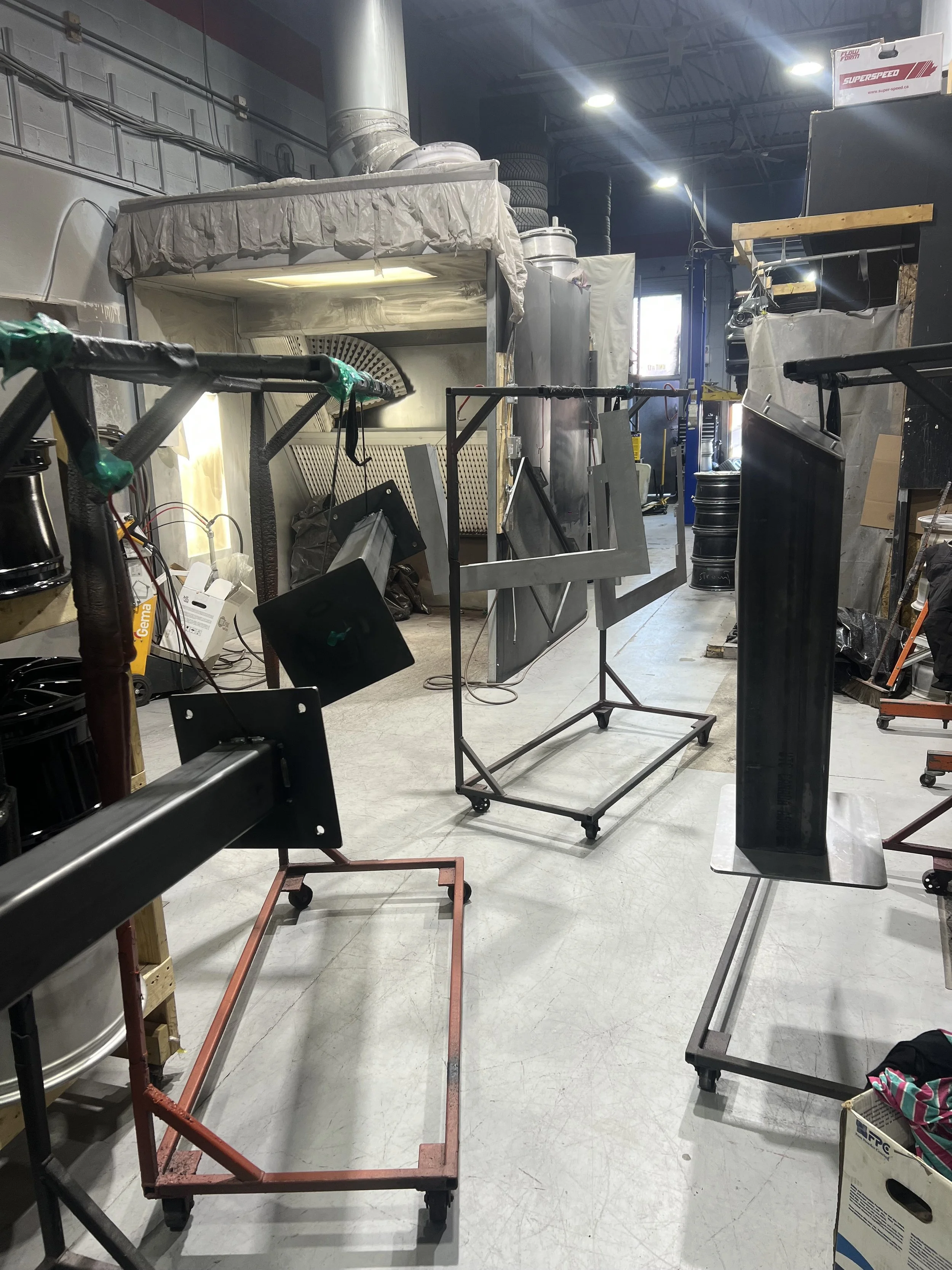 Workshop with metal frames and equipment, partially assembled tables, and workshop tools in a garage or industrial space.