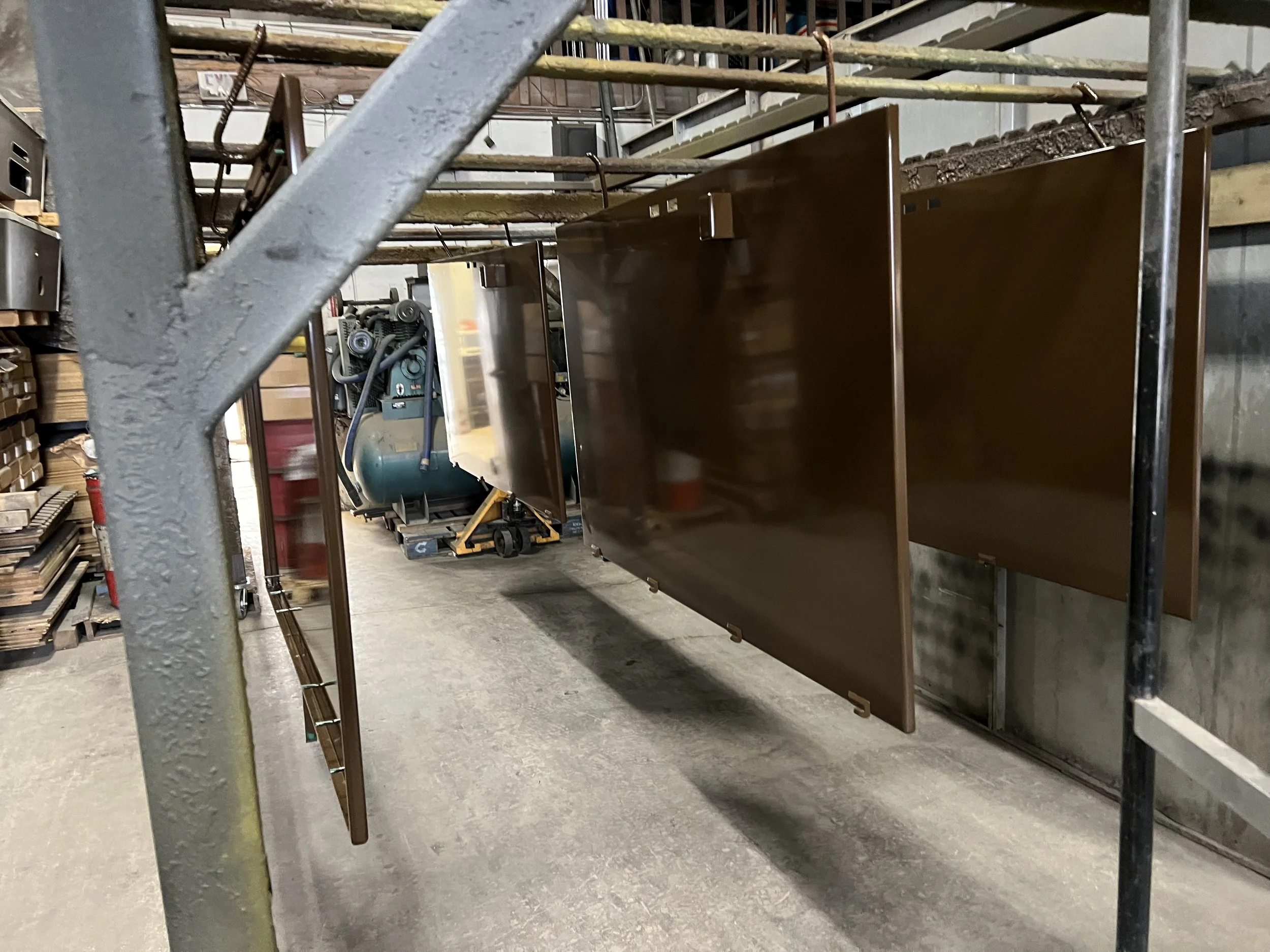 Metal panels hanging on a scaffolding inside a workshop, with tools and equipment in the background.