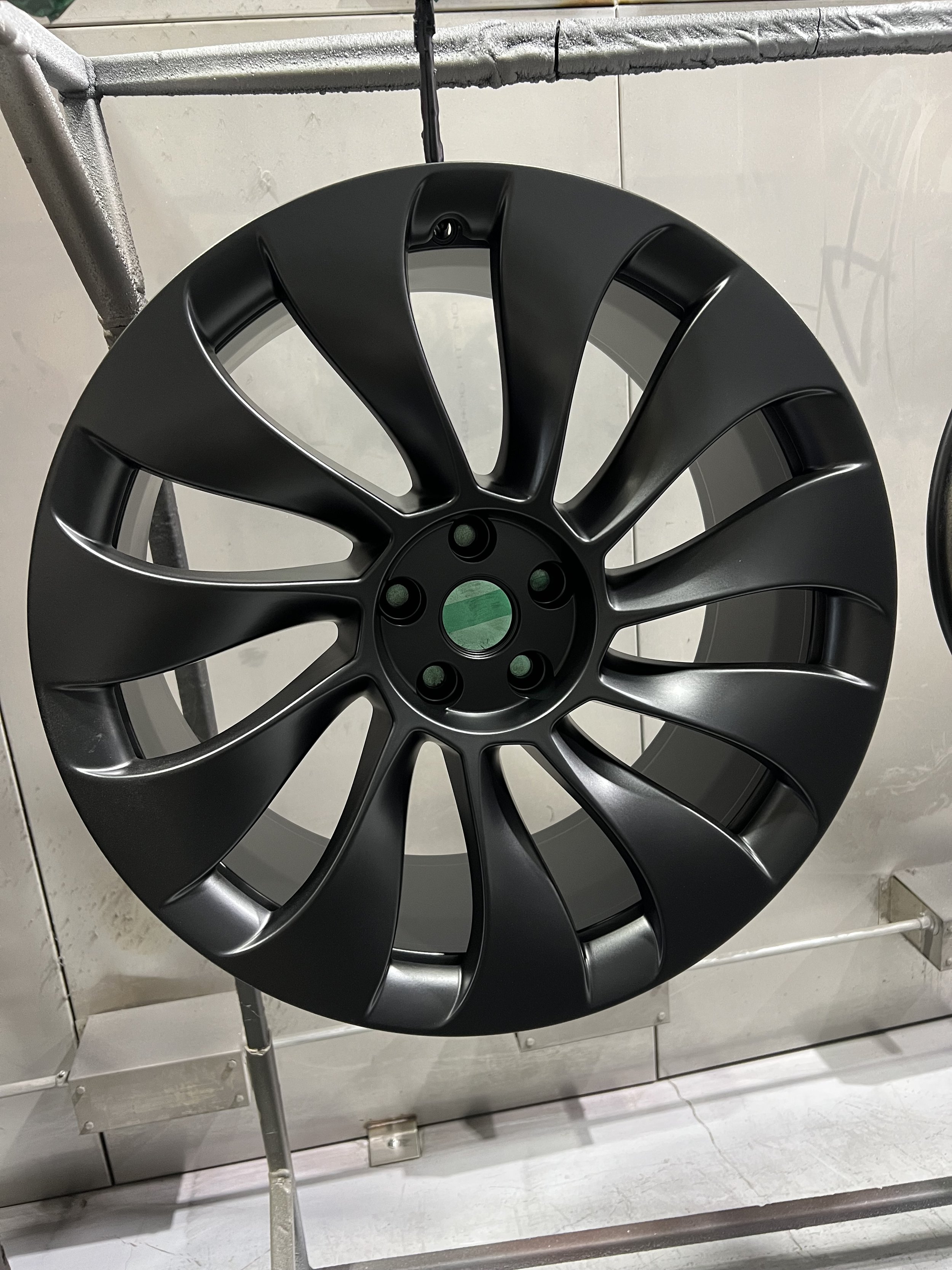 Black alloy car wheel rim displayed on a stand in a showroom or workshop.