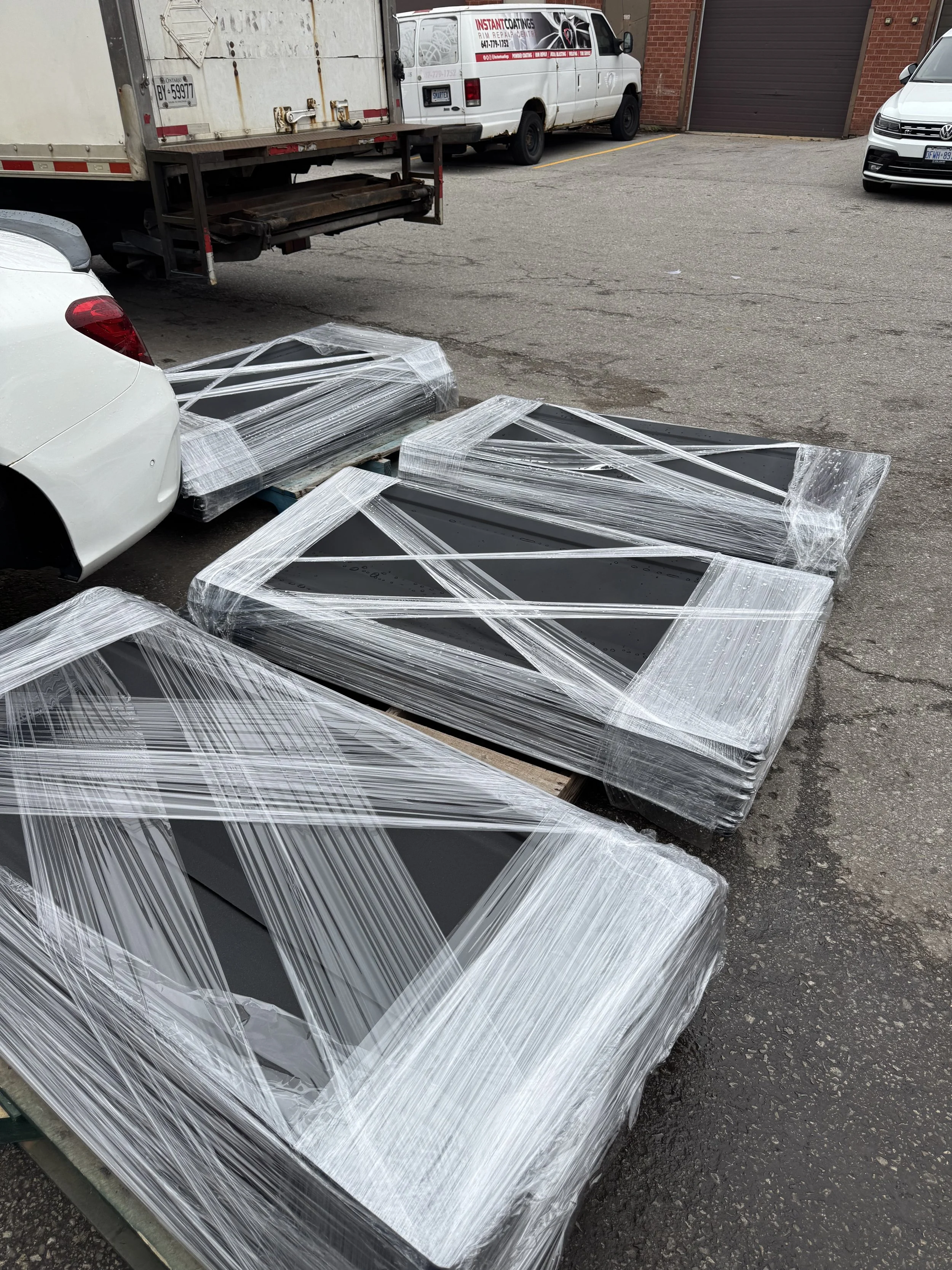Four black television displays wrapped in plastic and placed on wooden pallets in an outdoor parking lot.