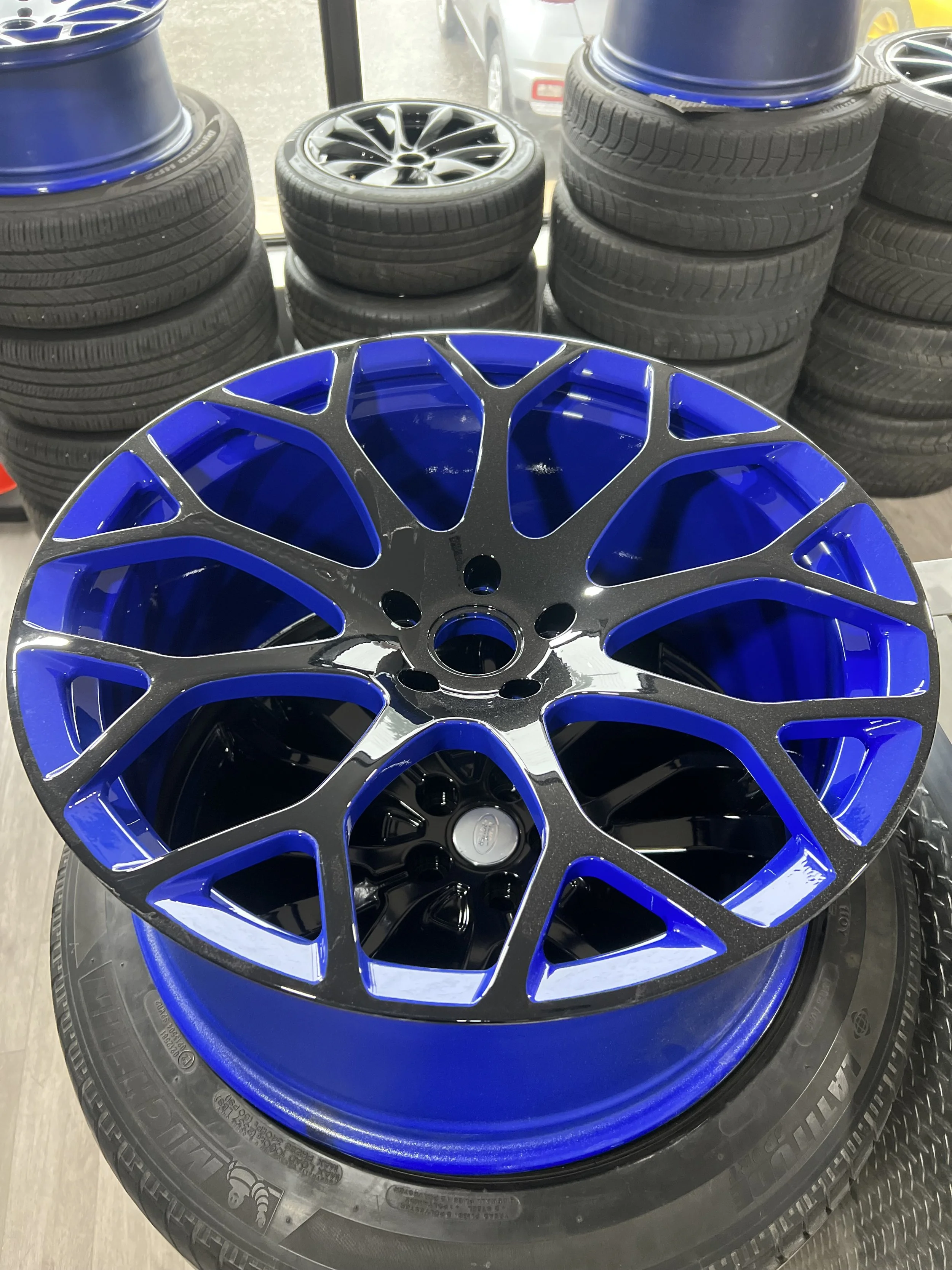 A blue and black automotive wheel rim placed on top of a tire near a display of other car wheels and tires inside a store.