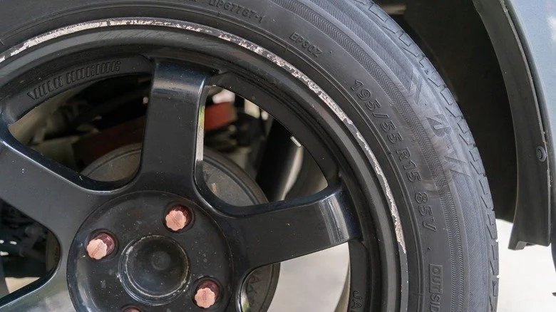 A black wire-spoke car wheel with a Continental tire, lying on a wooden floor. The center cap displays the Maserati logo.