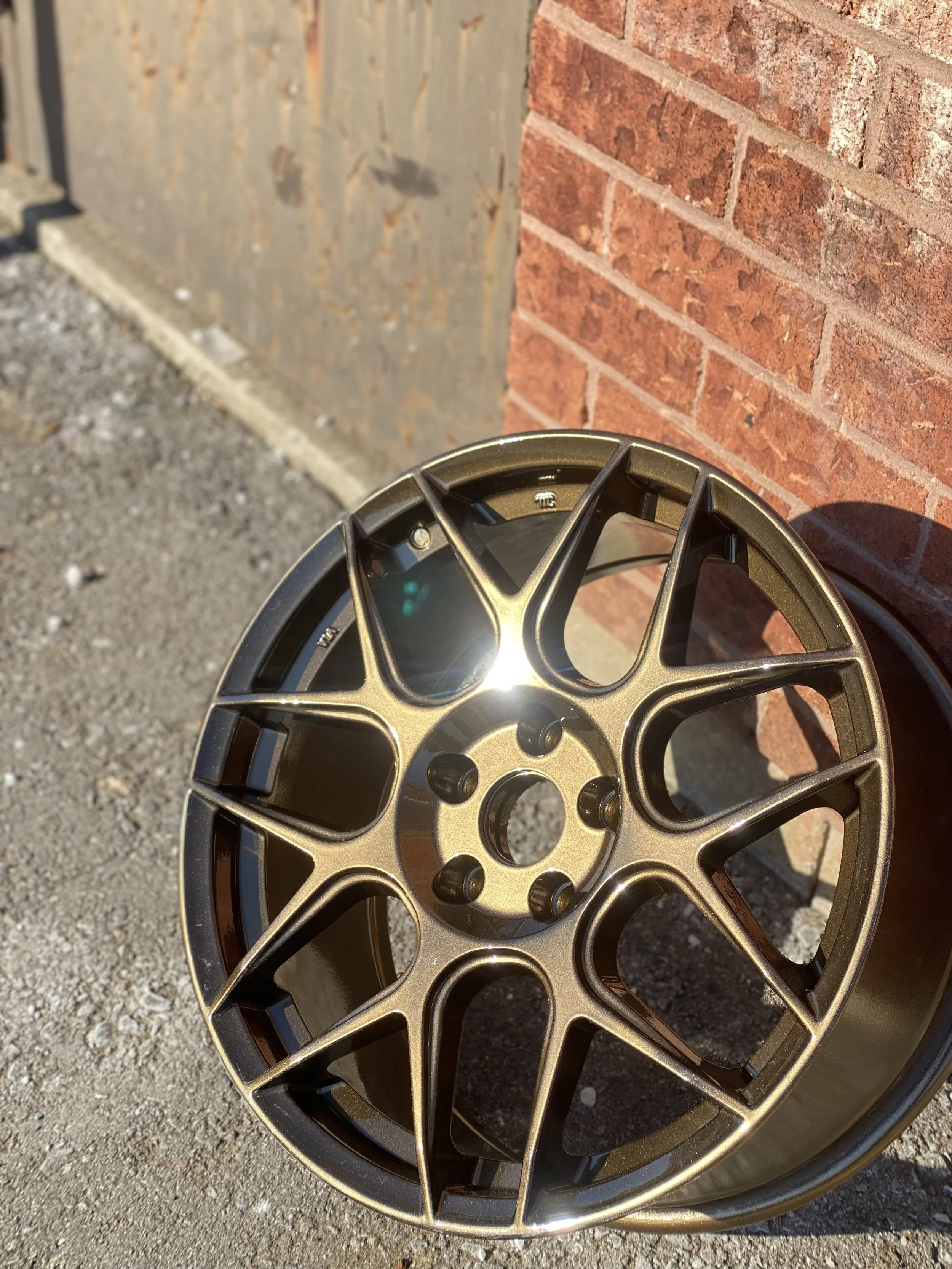 Car wheel rim leaning against a wall with a brick and wood surface in the background.
