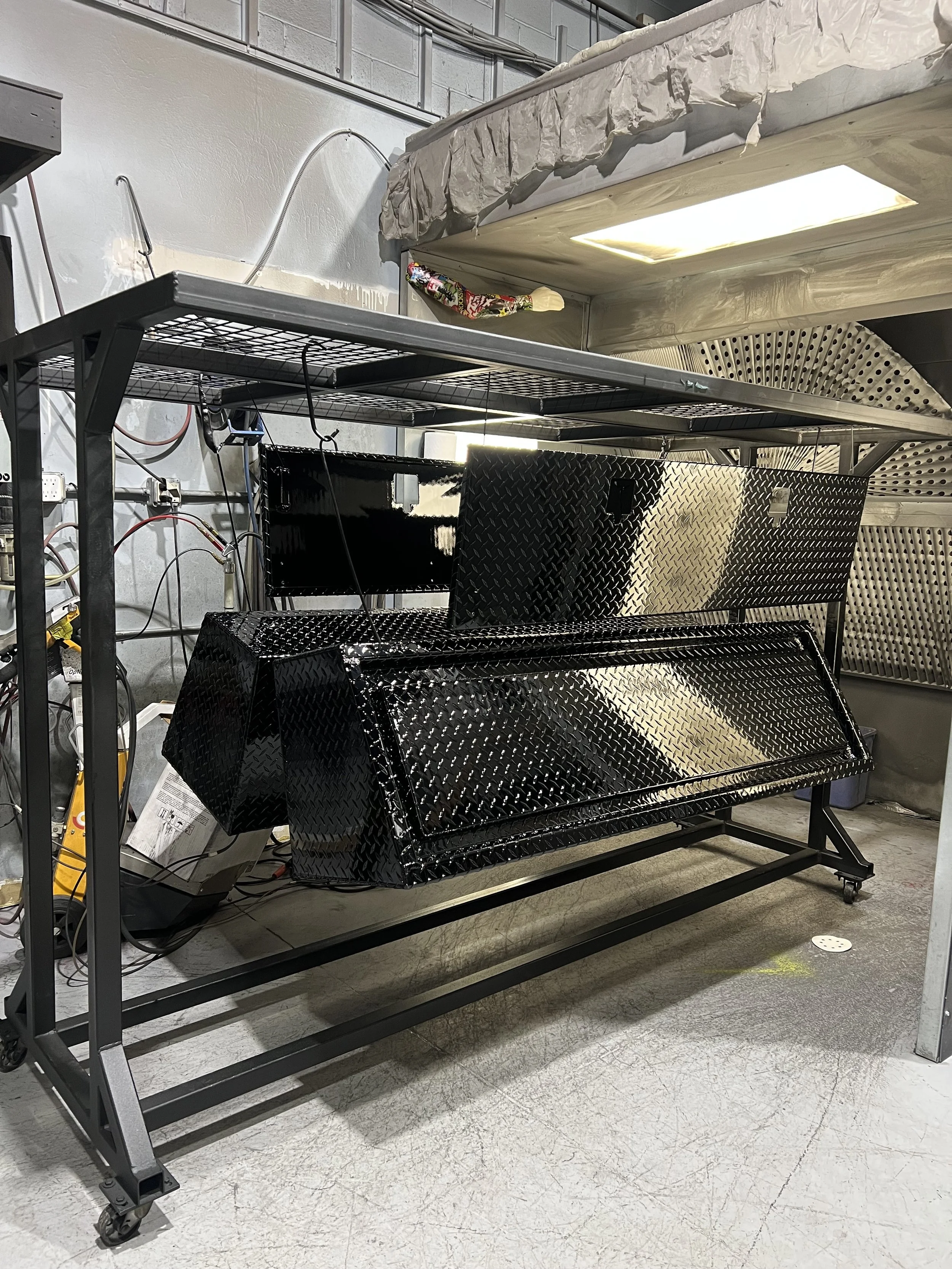 Metal work station with a black diamond plate cover, placed below a metal shelving unit in a workshop or industrial setting.