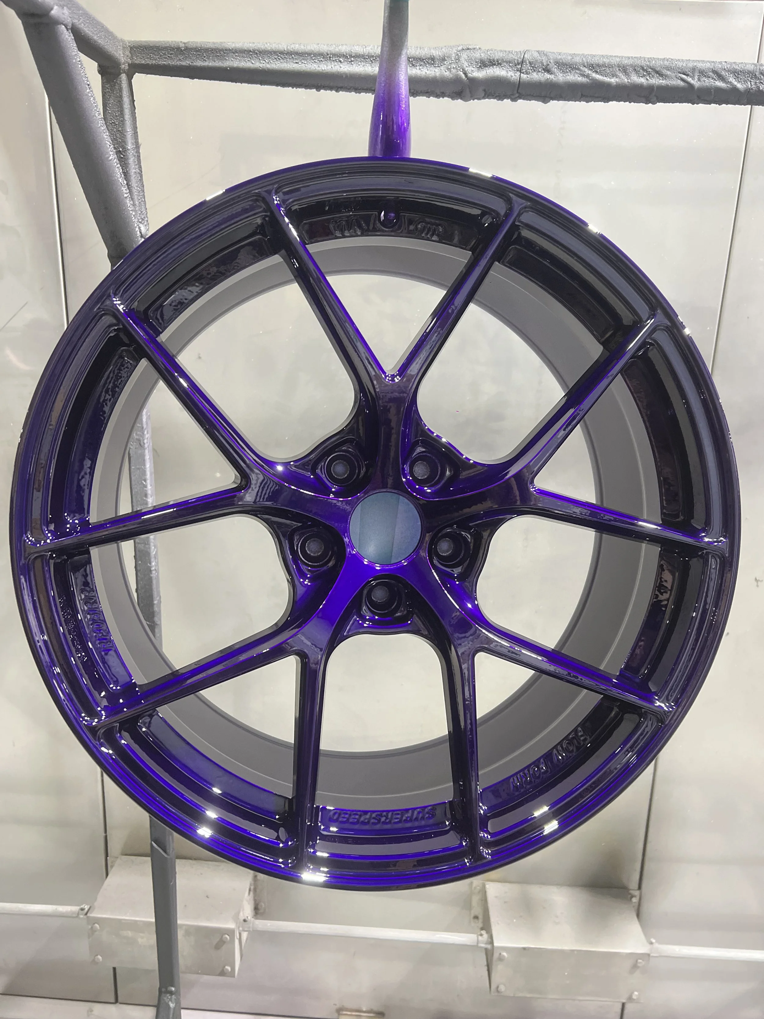 A painted alloy wheel rim with a purple finish, mounted on a display stand, with a white tiled background.