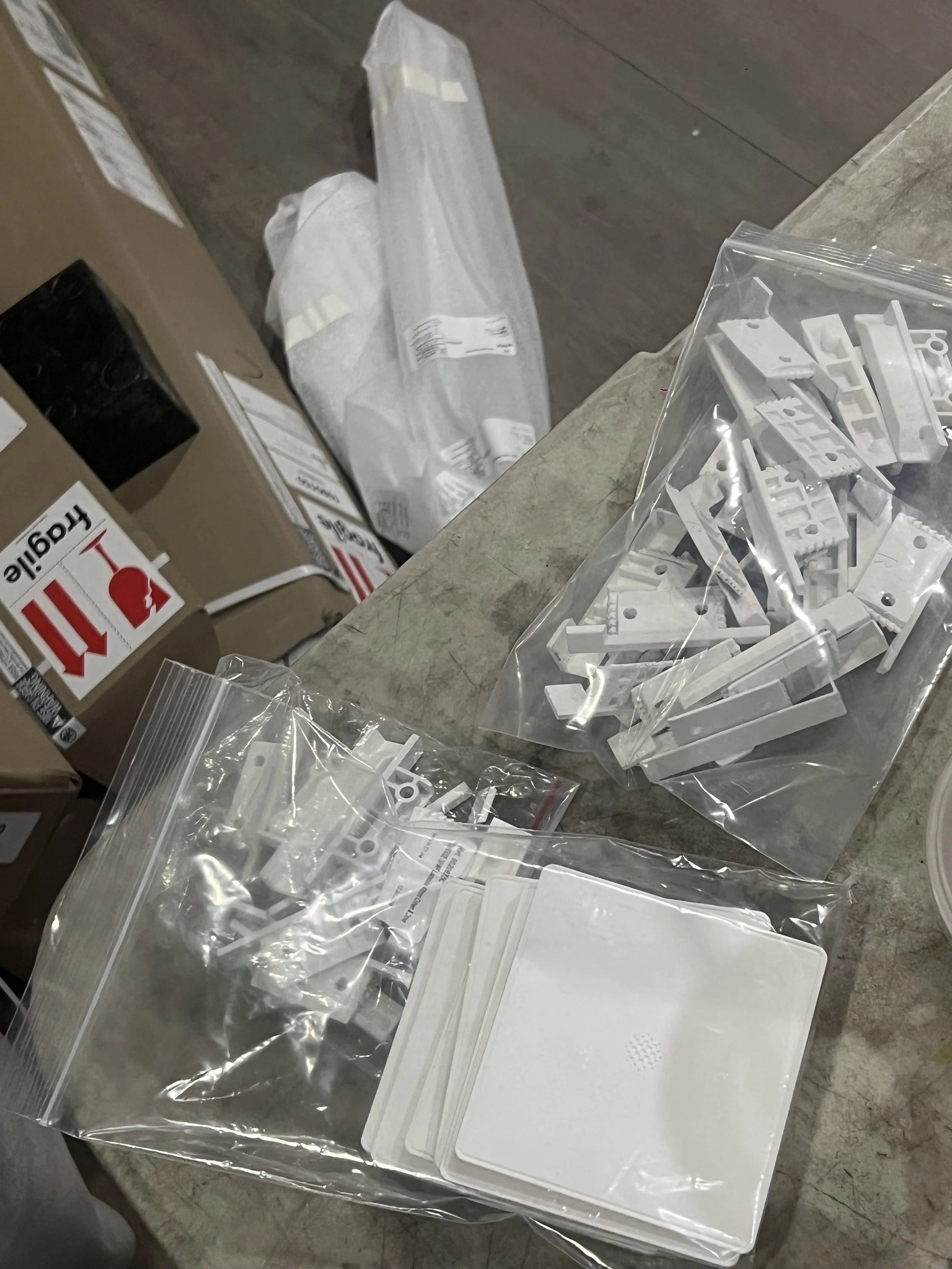 Electrical components and wiring connectors in plastic bags on a table, with a boxed item labeled 'Fragile' nearby.
