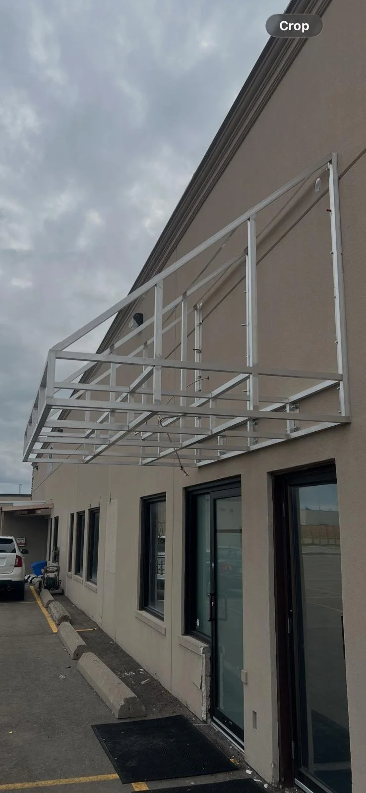 Metal framework for a balcony or storefront addition attached to the exterior wall of a building, with windows and a door below.