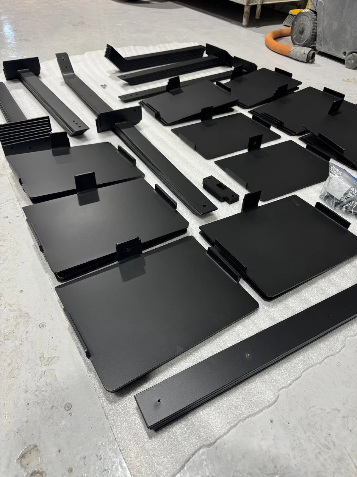 Various black metal components laid out on a white surface, possibly parts for assembly or construction.