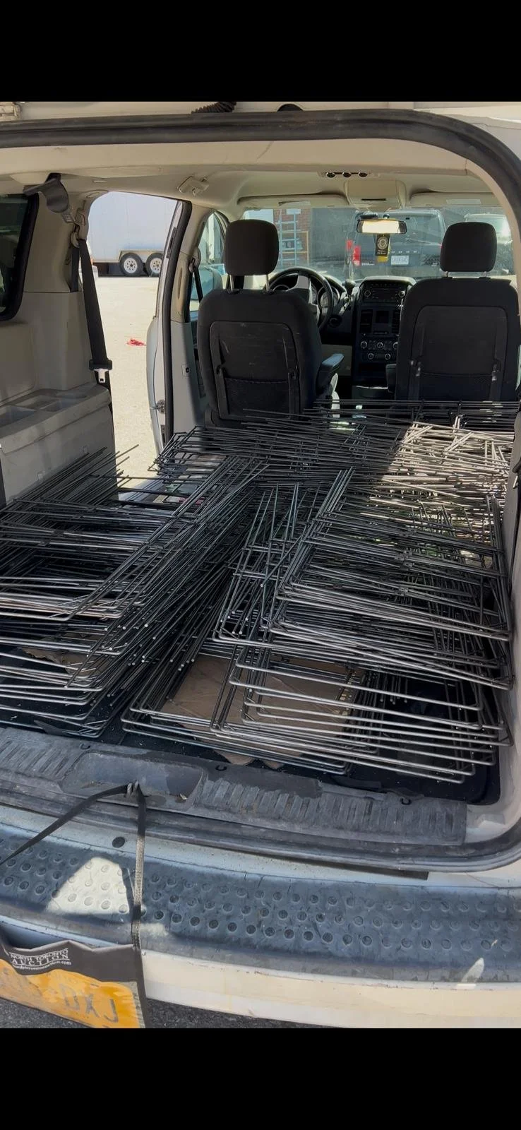 The back of a van filled with metal racks, with some racks stacked on each other, parked in a lot.