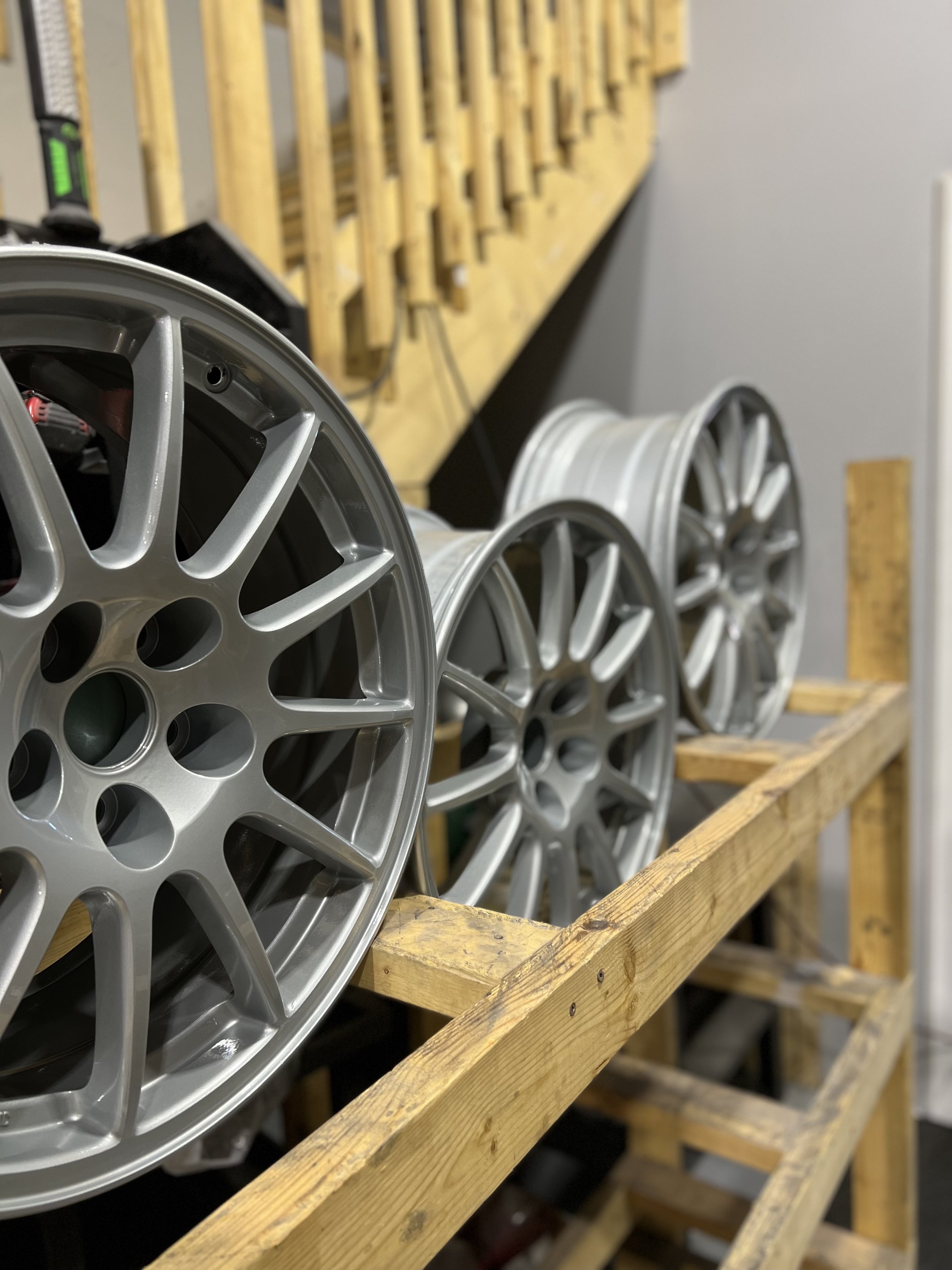 A row of silver alloy wheels on a wooden workbench in a workshop.