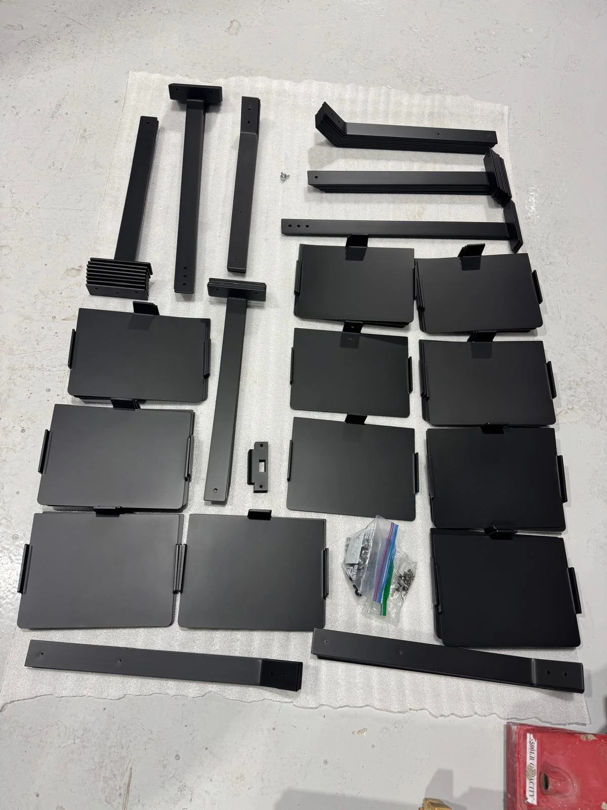 Disassembled black metal or plastic mounting brackets and panels laid out on a white surface.