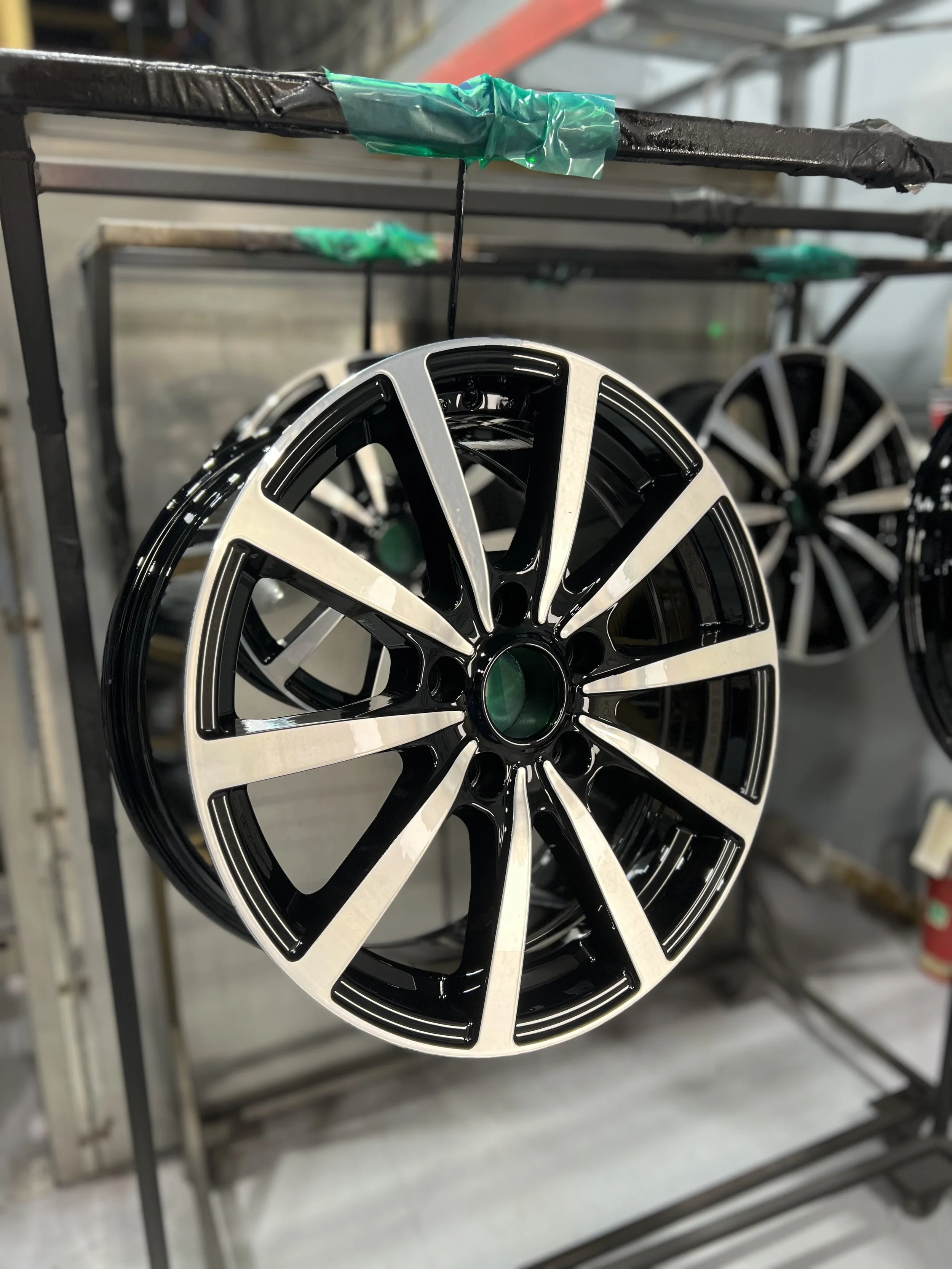 A black and silver alloy wheel rim hanging in a workshop or manufacturing setting.