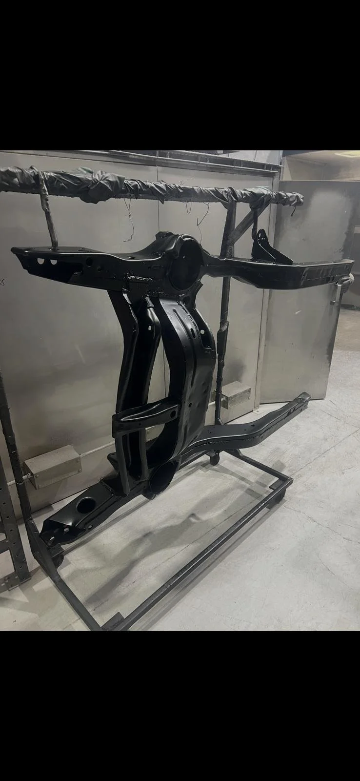 A black painted car chassis mounted on a metal stand in a workshop.