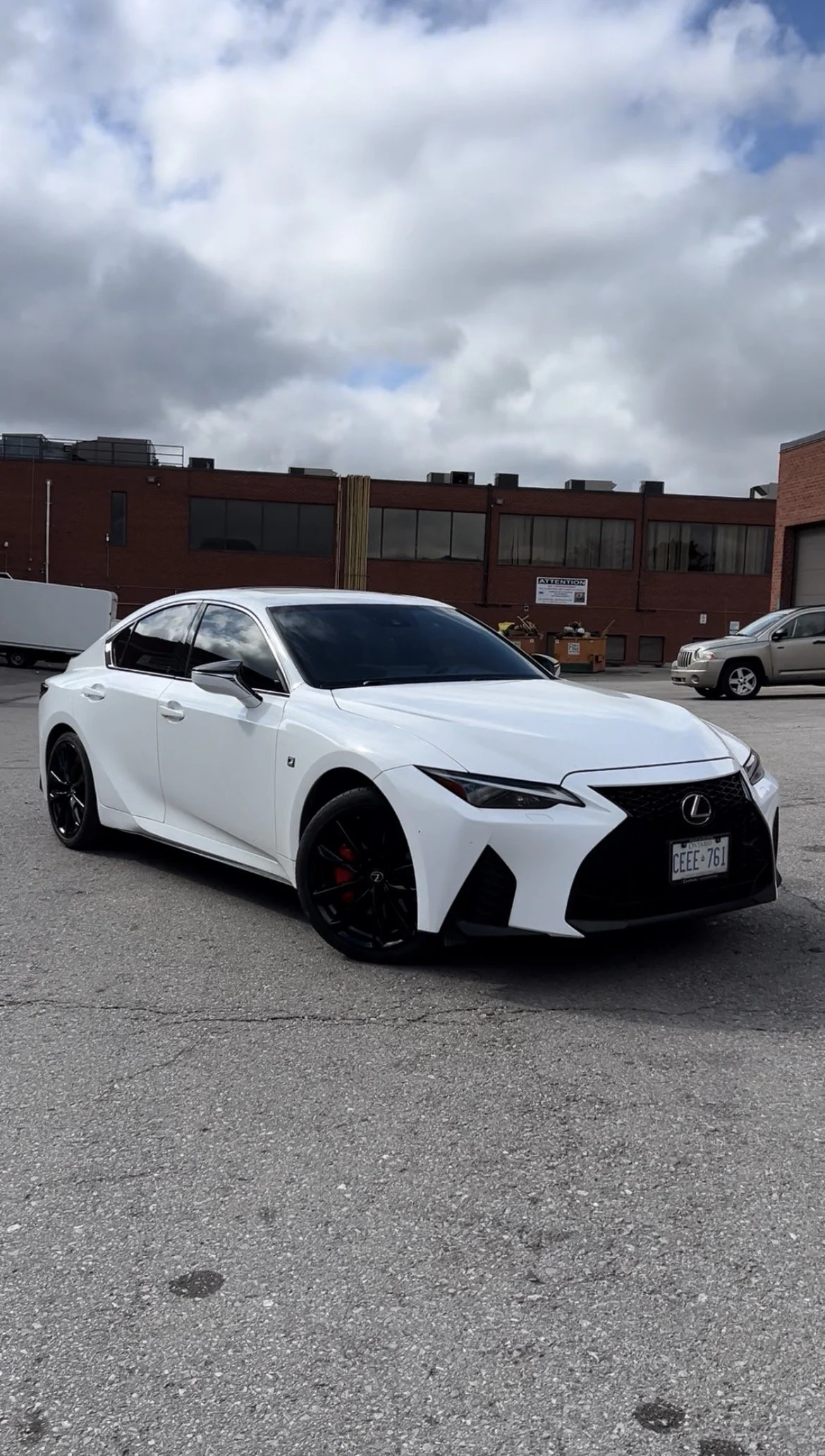 A white Lexus sports sedan with black wheels and red brake calipers, parked in an outdoor lot under cloudy skies.