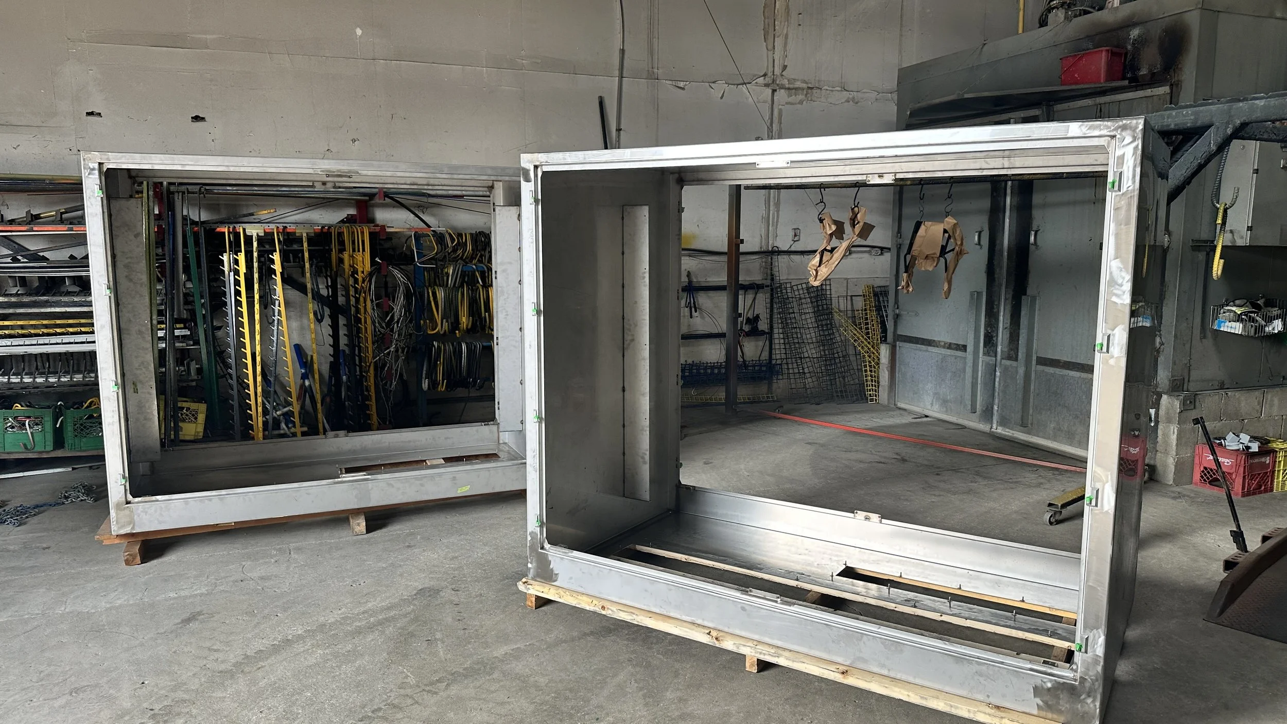 Two large empty metal frames in an industrial setting, with tools and equipment on shelves and walls in the background.