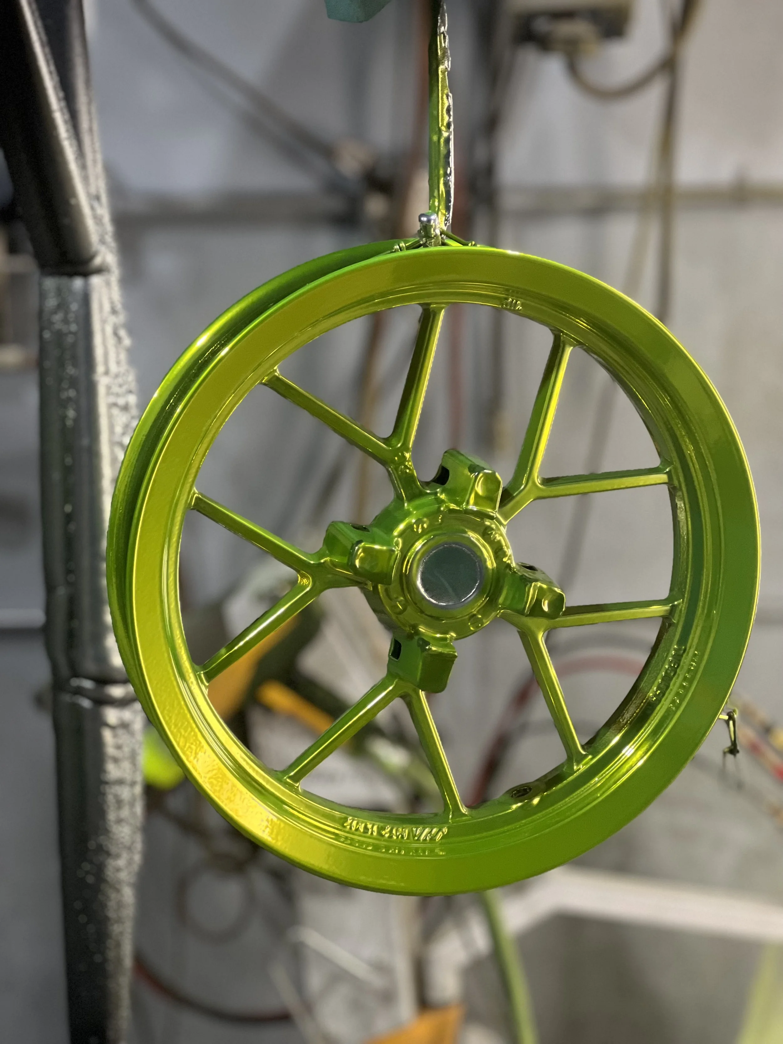 Close-up of a yellow metallic wheel or gear, hanging from a hook in an industrial or workshop setting.