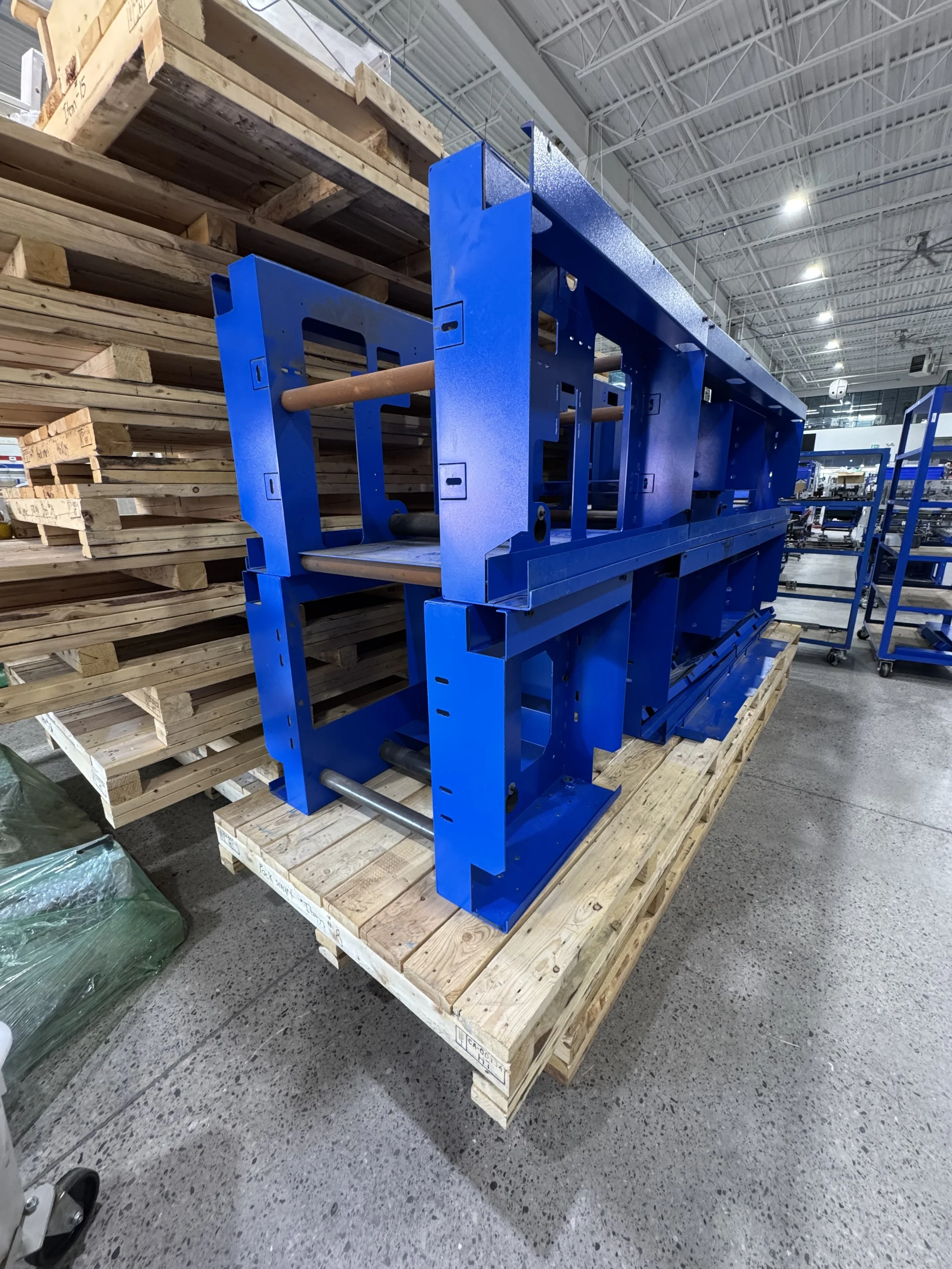 Blue industrial machine frame on wooden pallet in a warehouse.