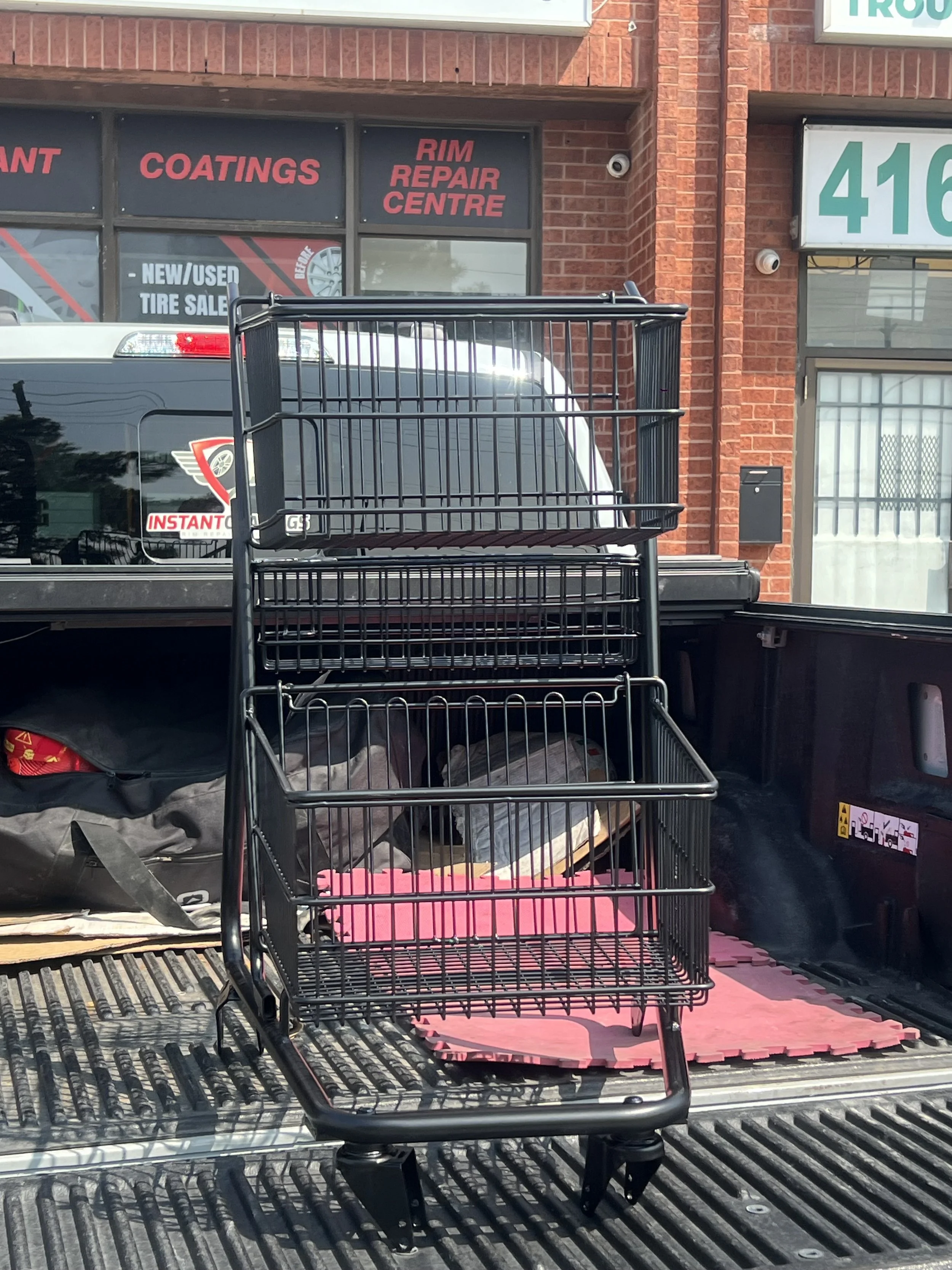 Black metal shopping cart placed in truck bed in front of auto repair shop with brick exterior.