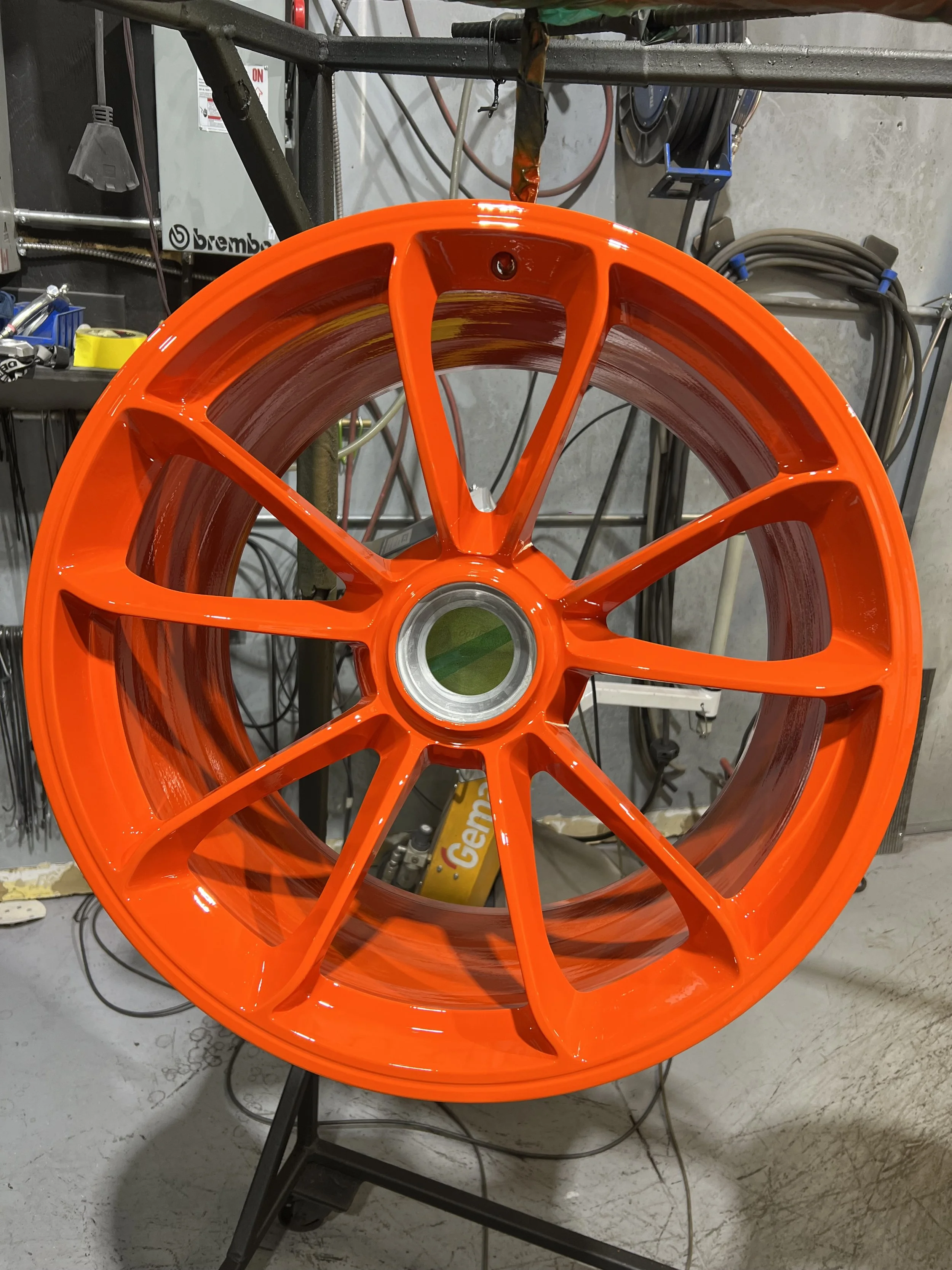 A bright orange wheel rim with multiple spokes, resting in a workshop or garage environment.