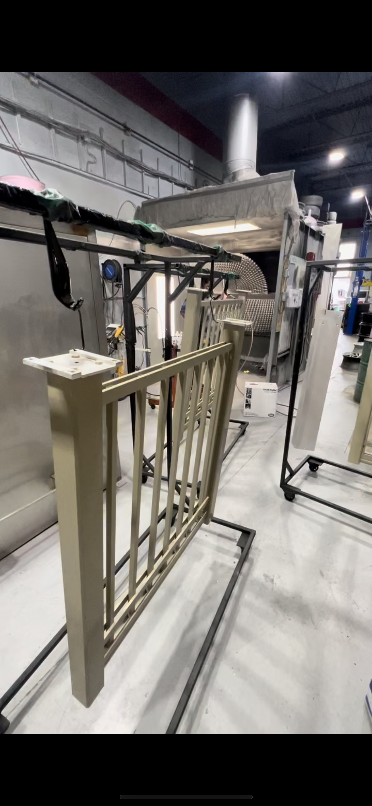 A retail or manufacturing setting with a beige wooden railing, metal framework, and large industrial equipment including a vent or filtration system. There are wires, tools, and boxes visible, indicating ongoing assembly or maintenance.