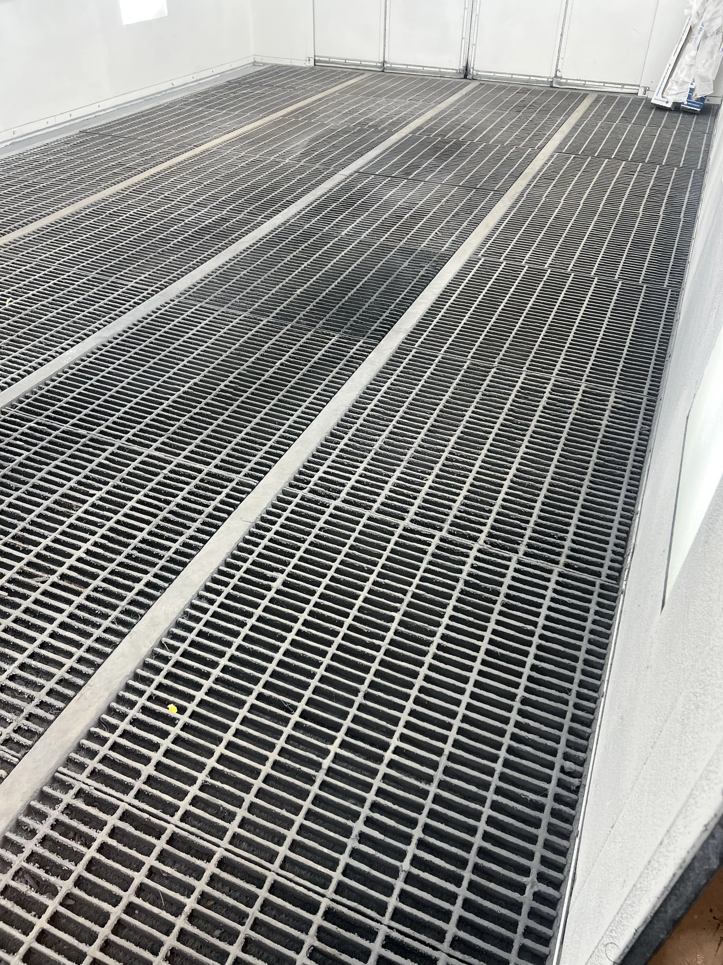 View of a clean, industrial metal grated floor inside a room with white walls and a white door.