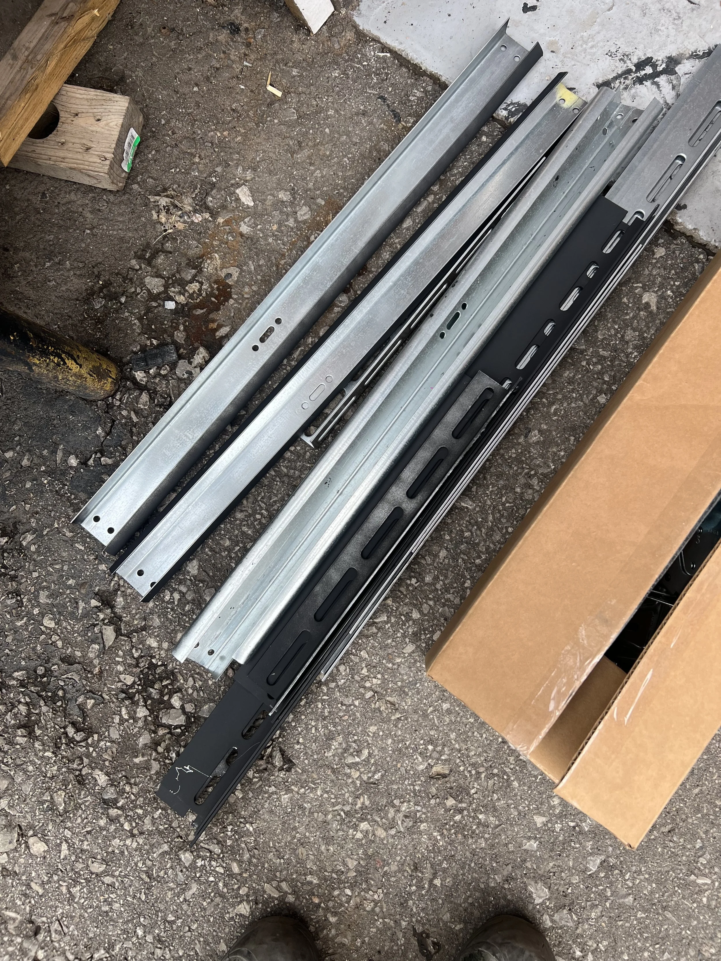 A collection of metal drawer slides and brackets on a concrete ground at a construction site.