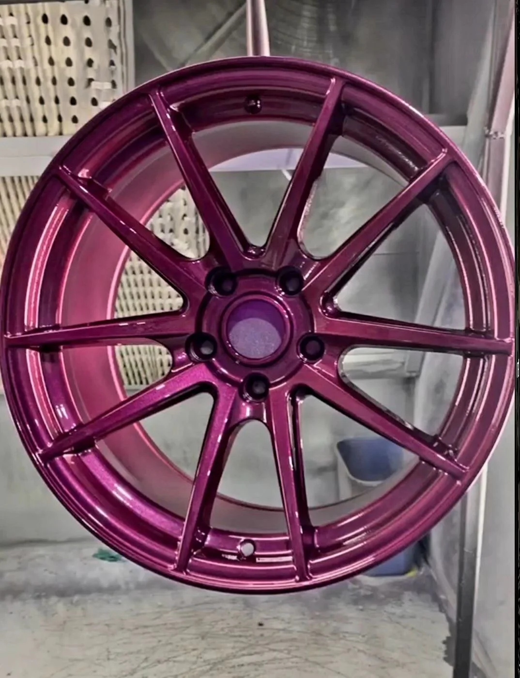 A pink, shiny, multi-spoke car wheel rim hanging in a workshop or garage.