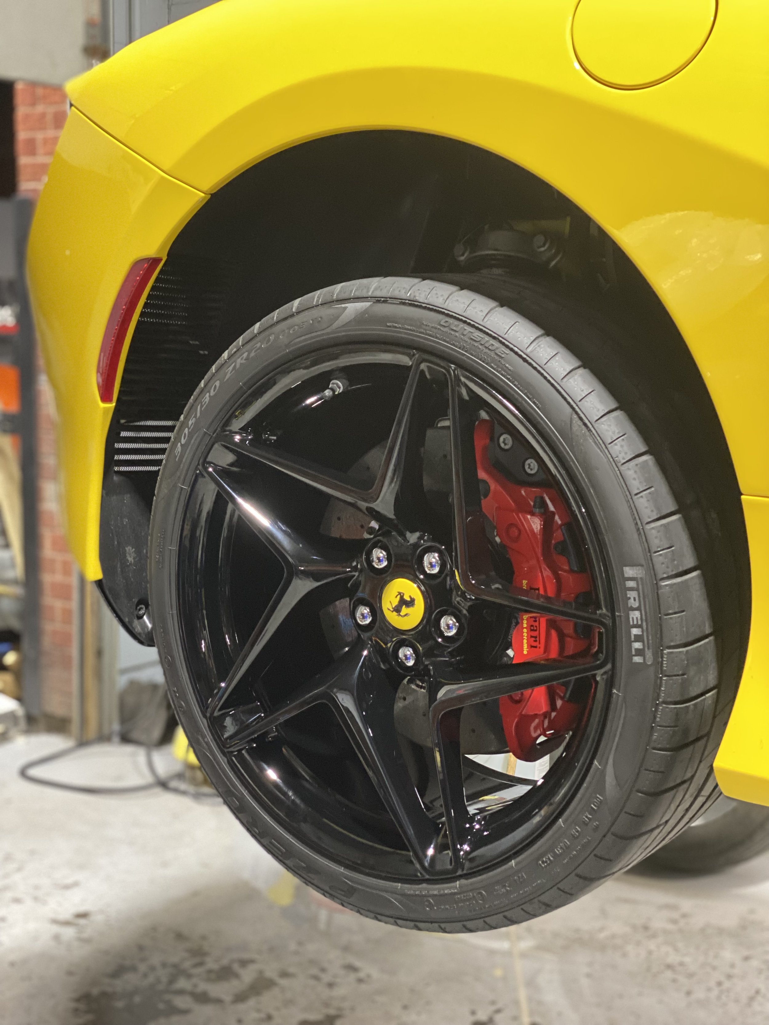 Close-up of the front wheel of a yellow Ferrari, showing a black alloy rim with a yellow Ferrari logo in the center, red brake caliper, and Pirelli tire.