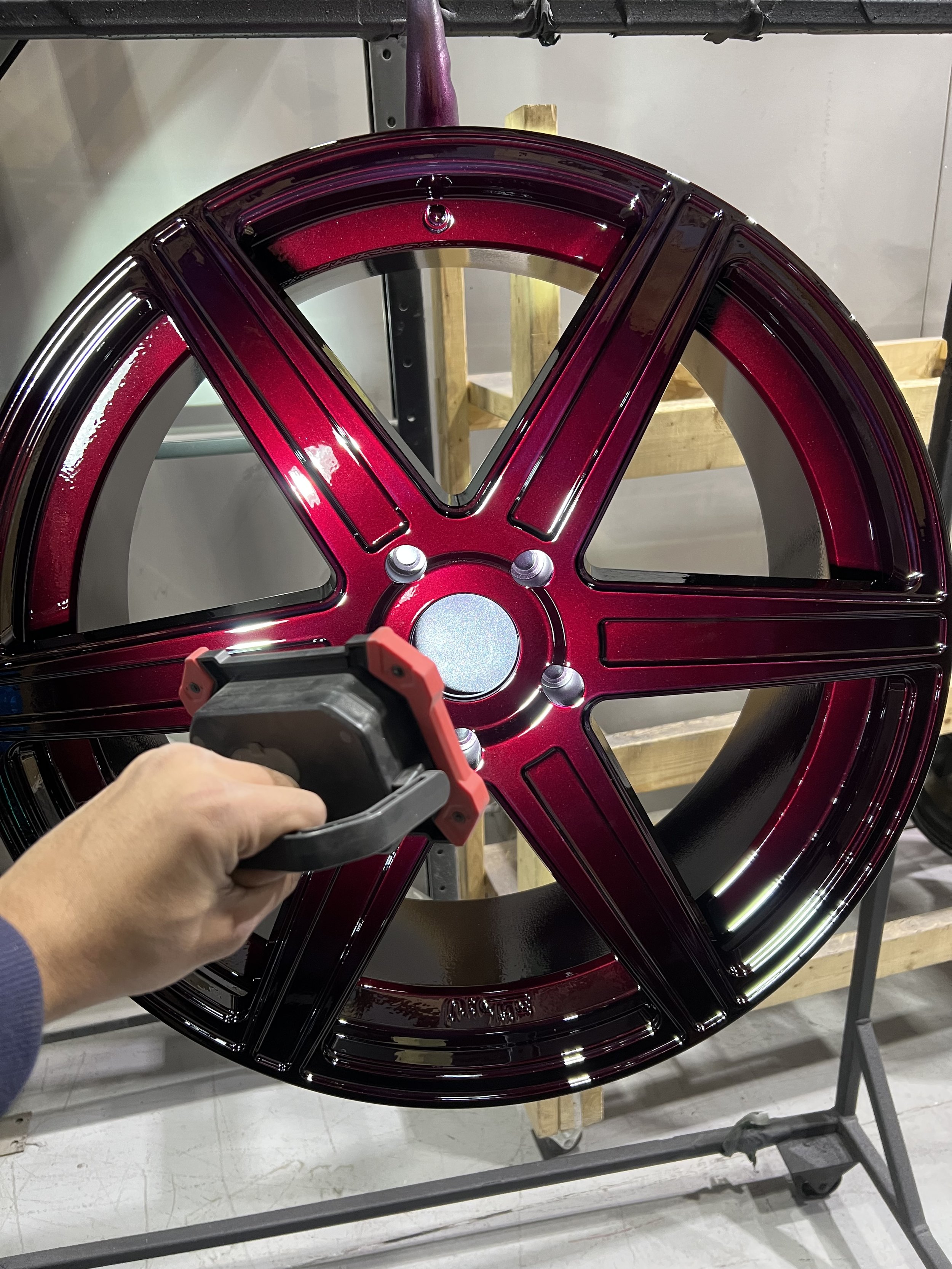 A person is spray painting a large, shiny, red and black wheel rim with a spray gun.