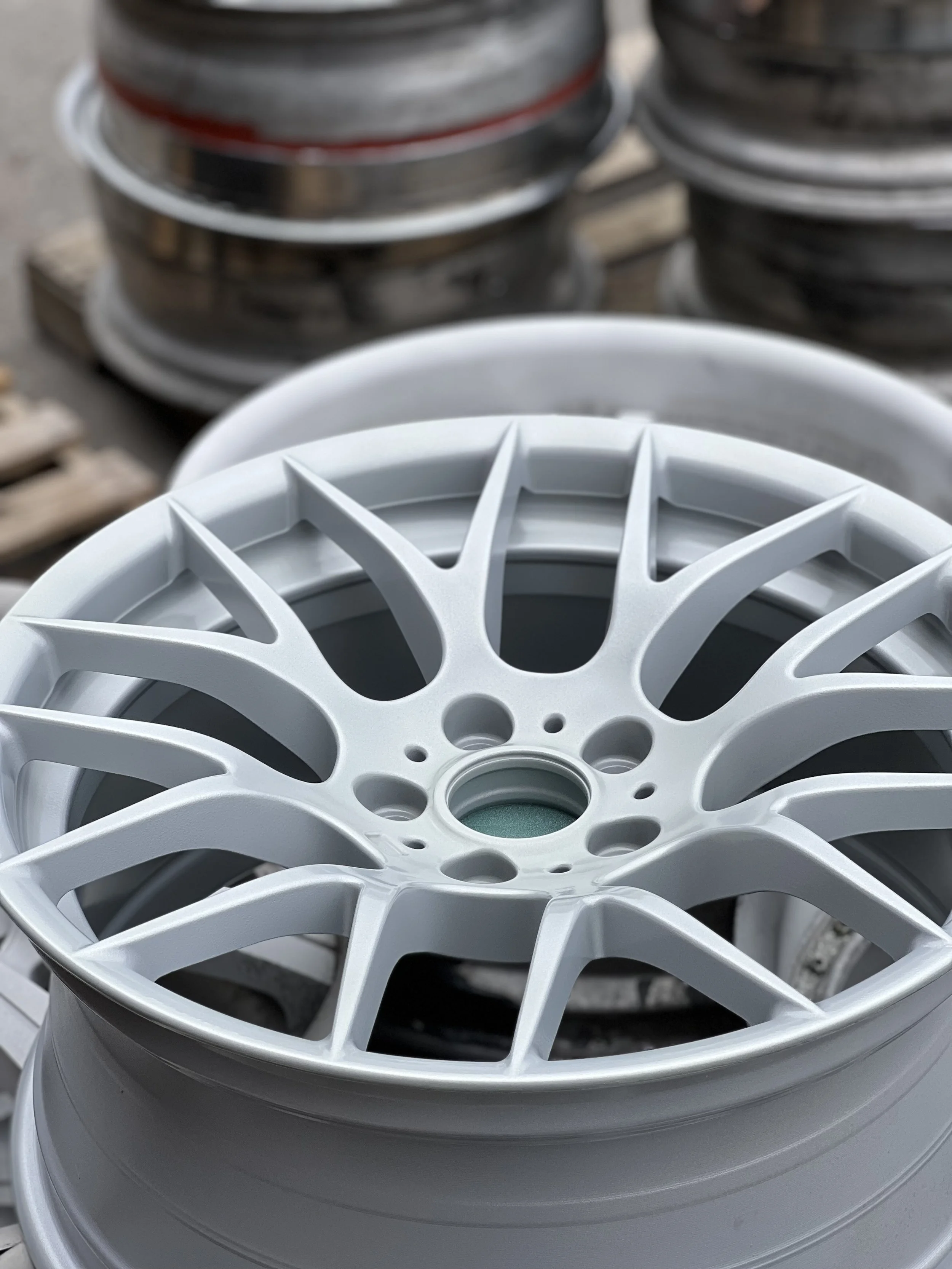 Close-up of a white car wheel rim with multiple spokes, with other wheels stacked in the background.