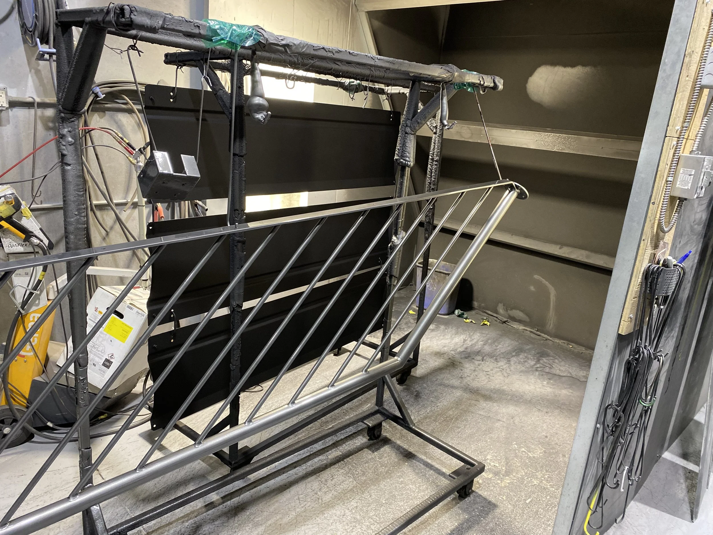 Steel construction rack with black panels and metal slats in a workshop setting, with tools and supplies on the side.