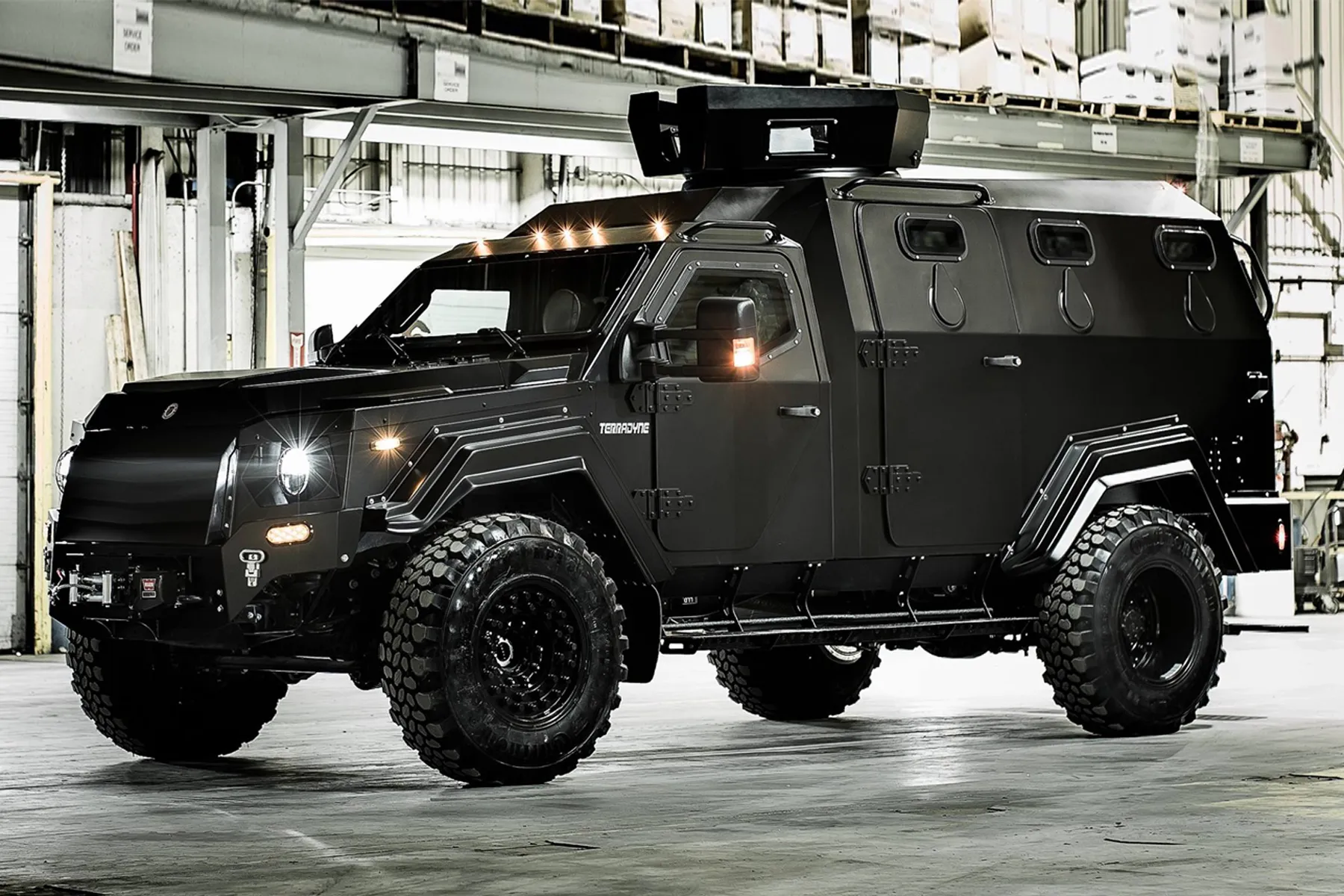 Black armored vehicle with rugged tires inside a warehouse or industrial building.