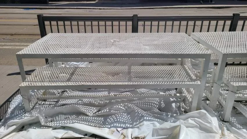 White outdoor table and matching benches on a patio, with a railing and street in the background.