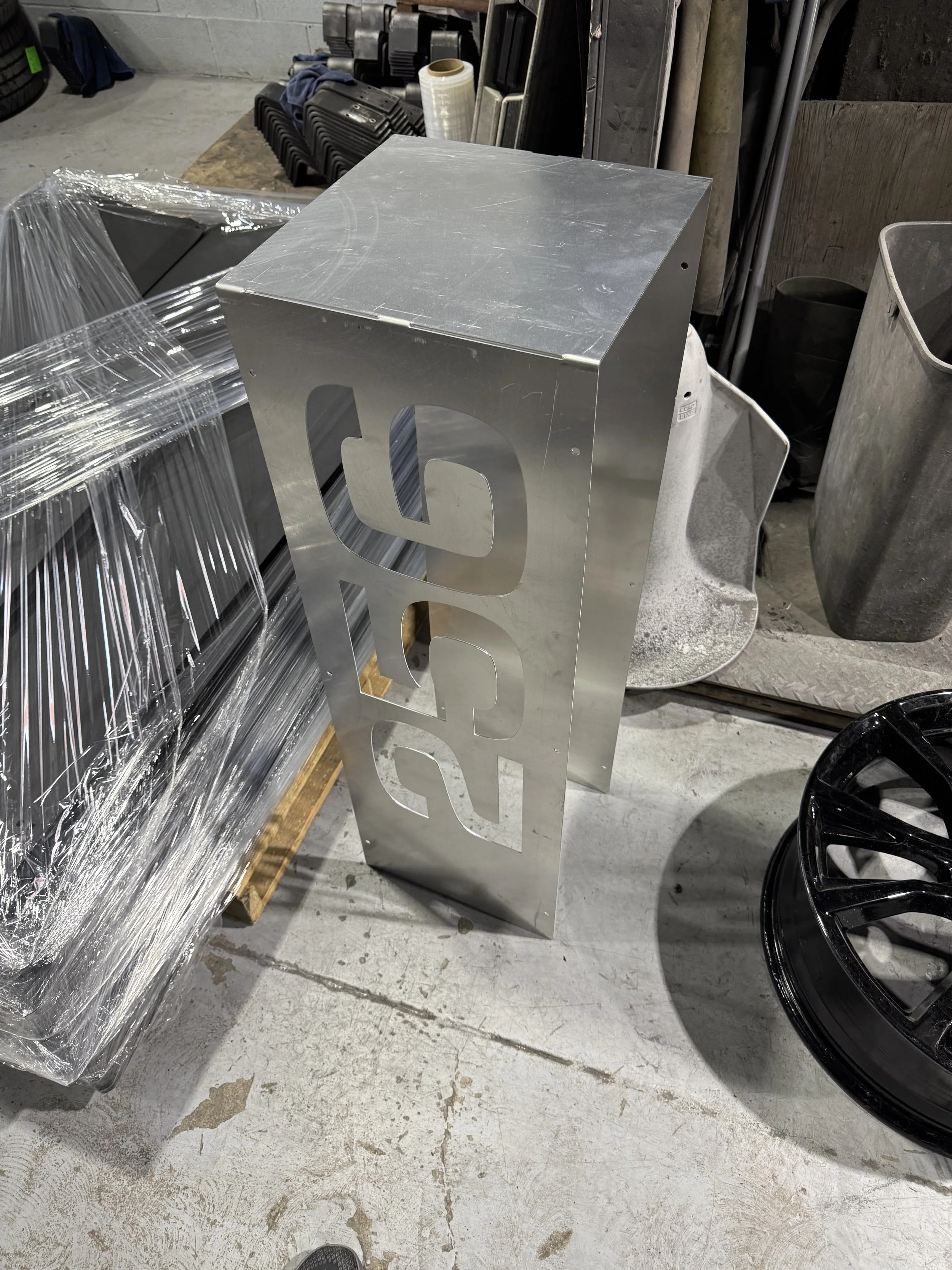 A metal sign with the word 'RUBY' cut out, leaning against a pallet in a warehouse or workshop.