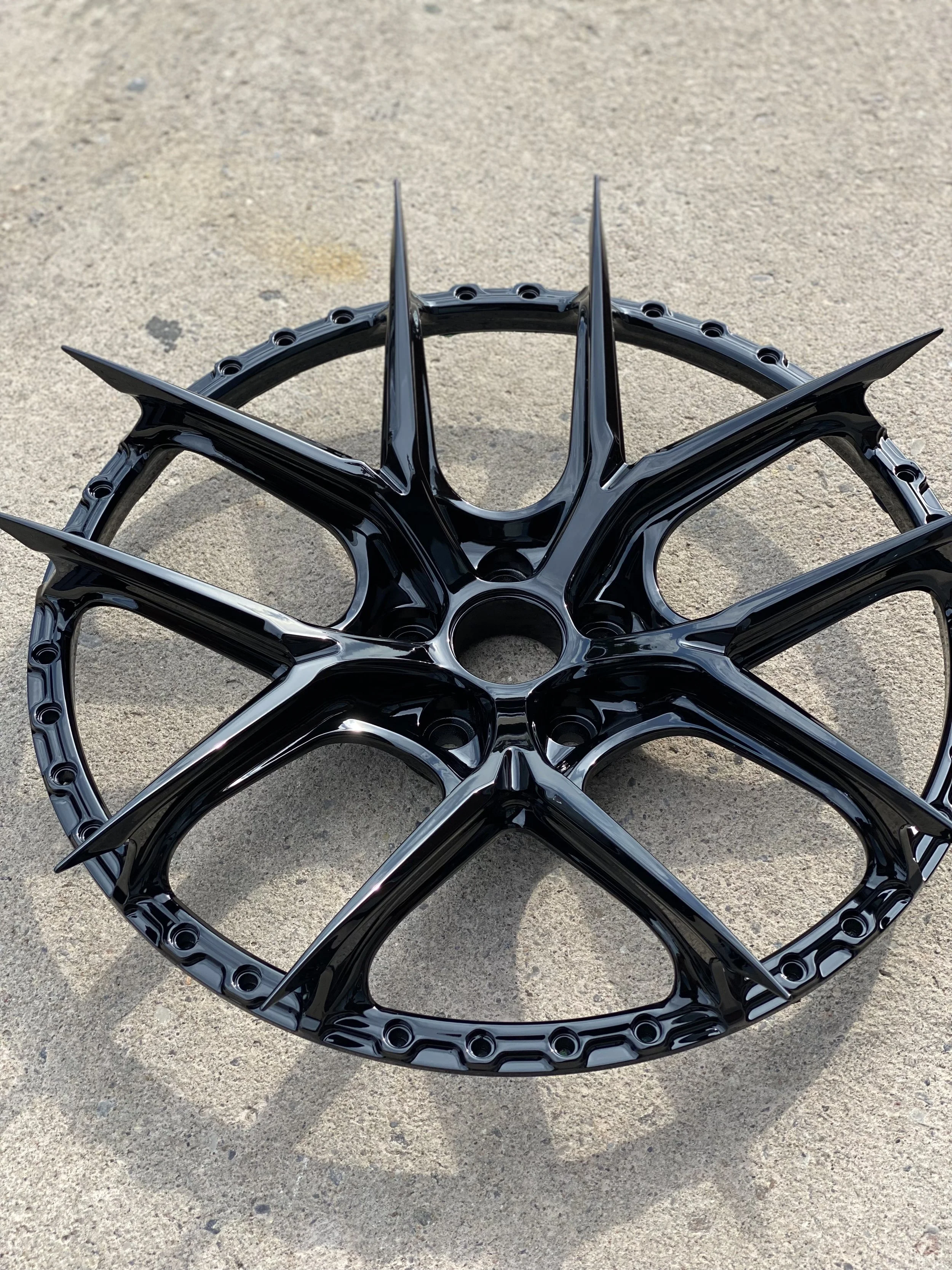 Black spiked bicycle or motorcycle wheel rim with a circular center and multiple sharp, pointed spokes, lying on concrete surface.