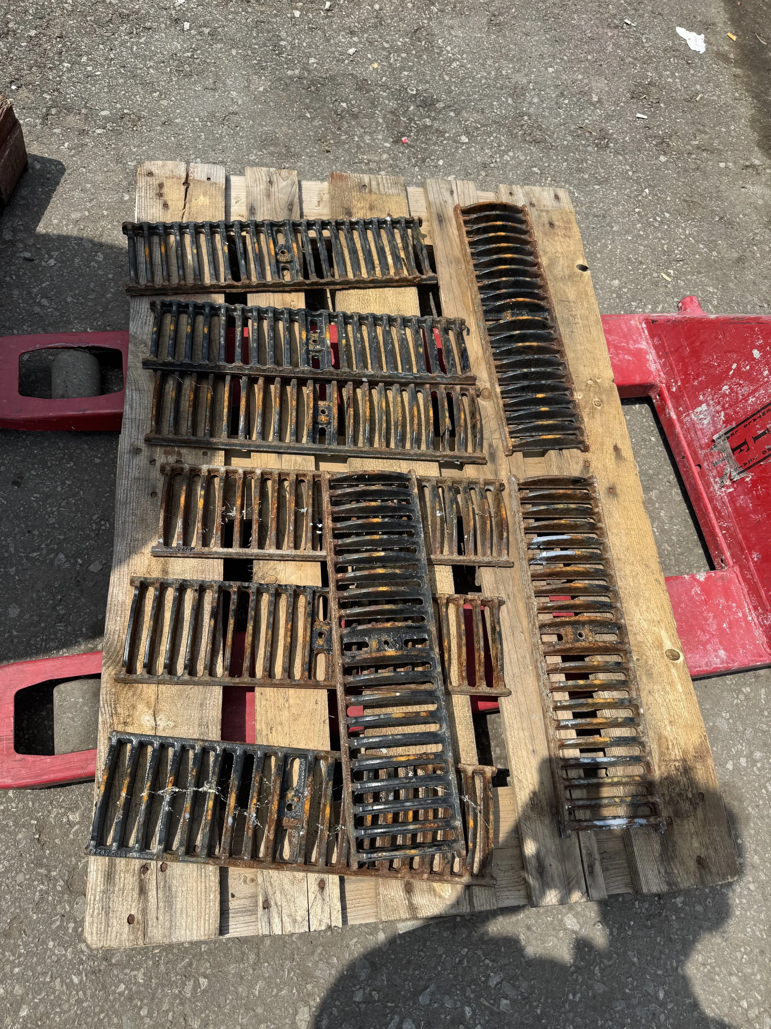 Several rusty metal grates and filters placed on a wooden pallet on an outdoor concrete surface.