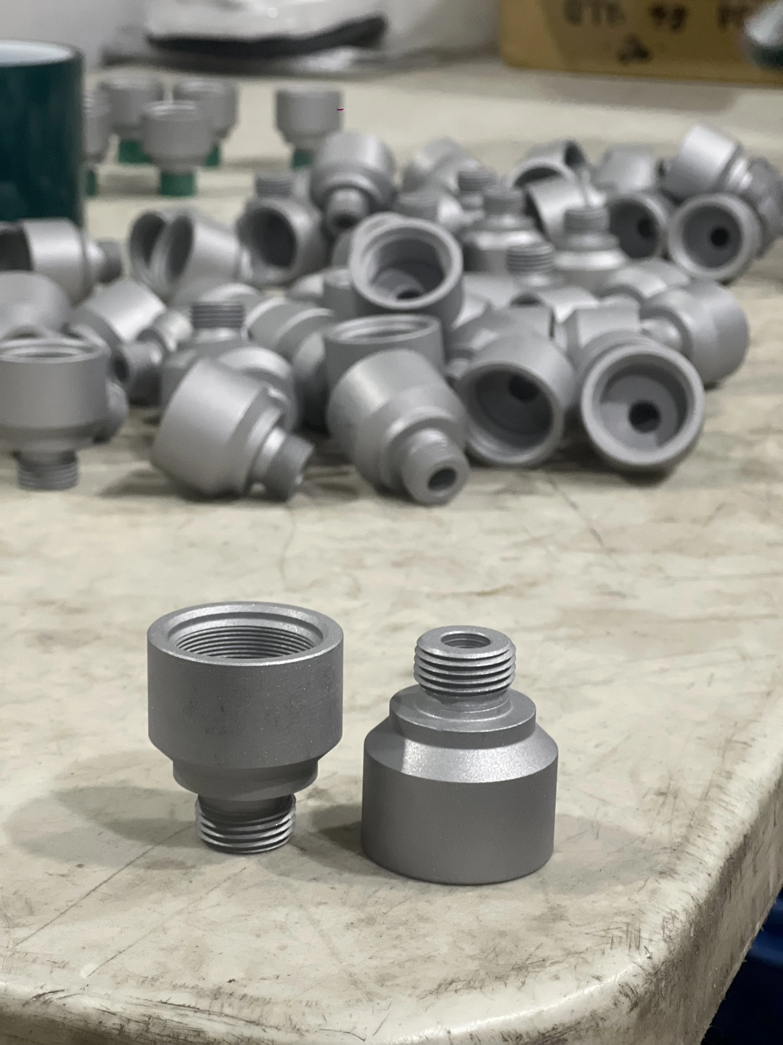 Close-up of metal fittings or connectors placed on a workbench, with many similar fittings scattered in the background.