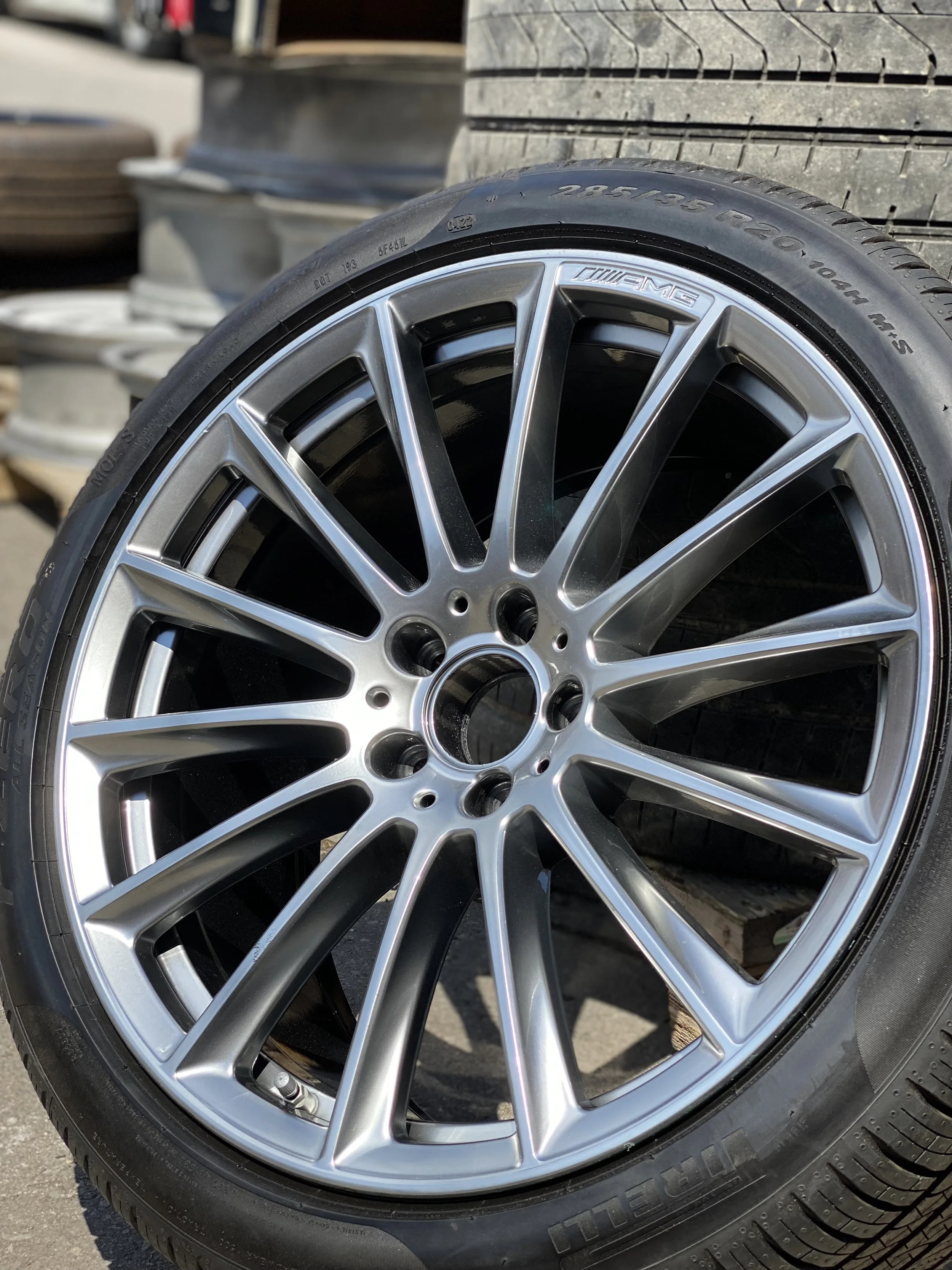 A close-up of a silver multi-spoke AMG alloy wheel with a tire mounted on it.