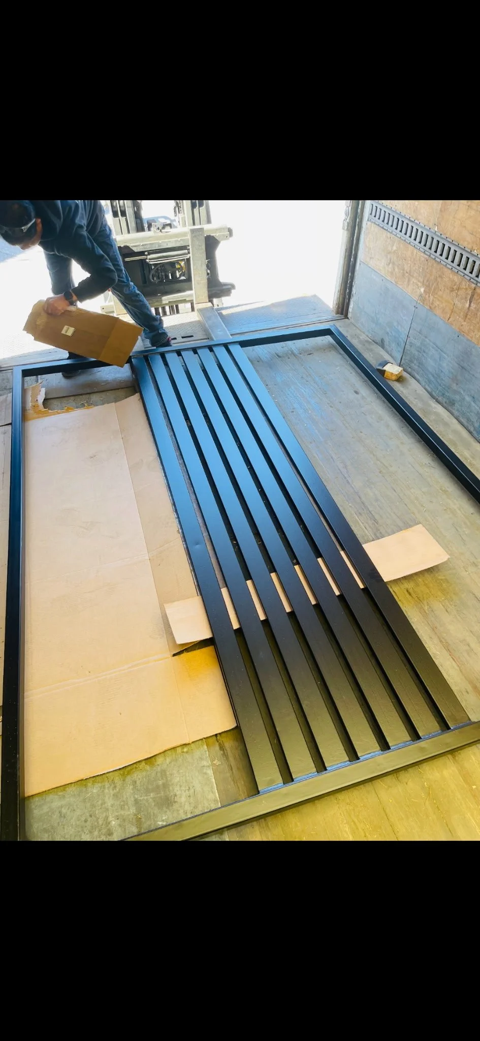 A person installing a black metal slatted bench inside a truck or moving vehicle.