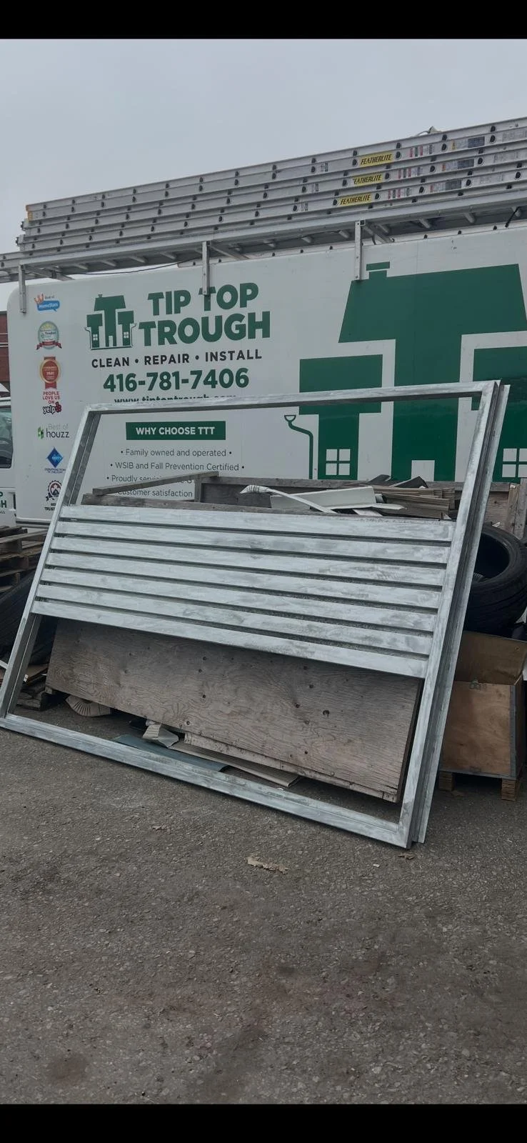 Metal frame leaning against a wooden structure, with a large truck labeled 'Tip Top Trough' in the background.