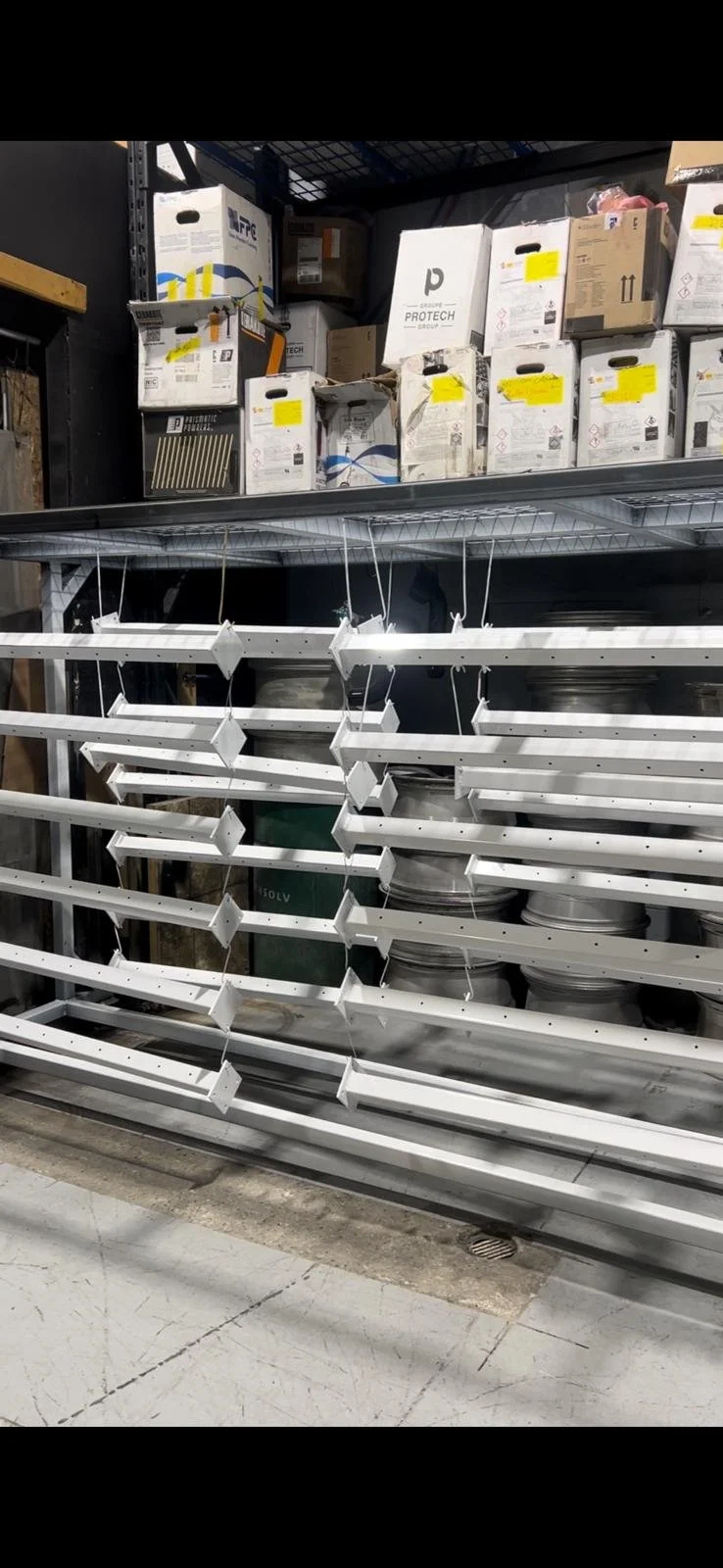 Empty metal shelving units in a warehouse with boxes and supplies on shelves in the background.
