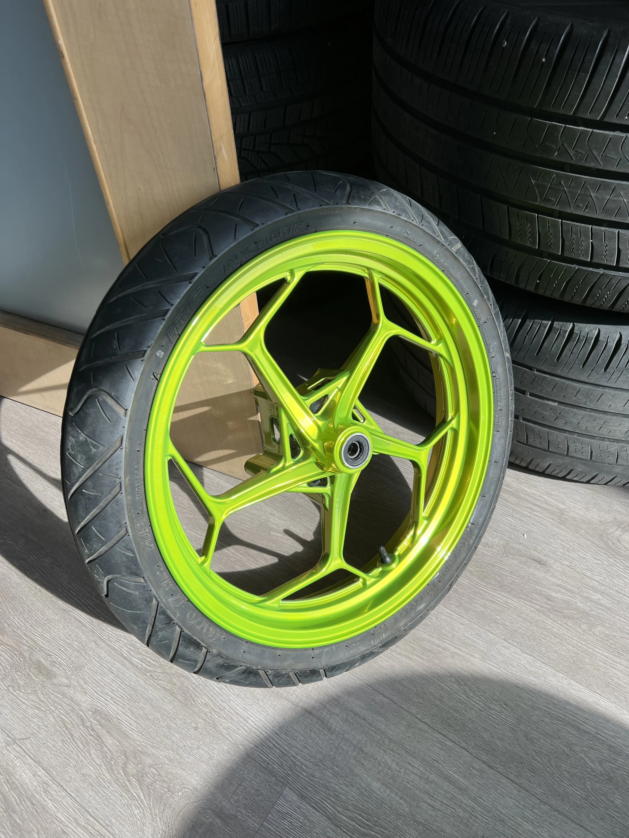 A bright yellow-green racing bicycle wheel with a low-profile tire, leaning against a wooden surface, with stacks of tires in the background.