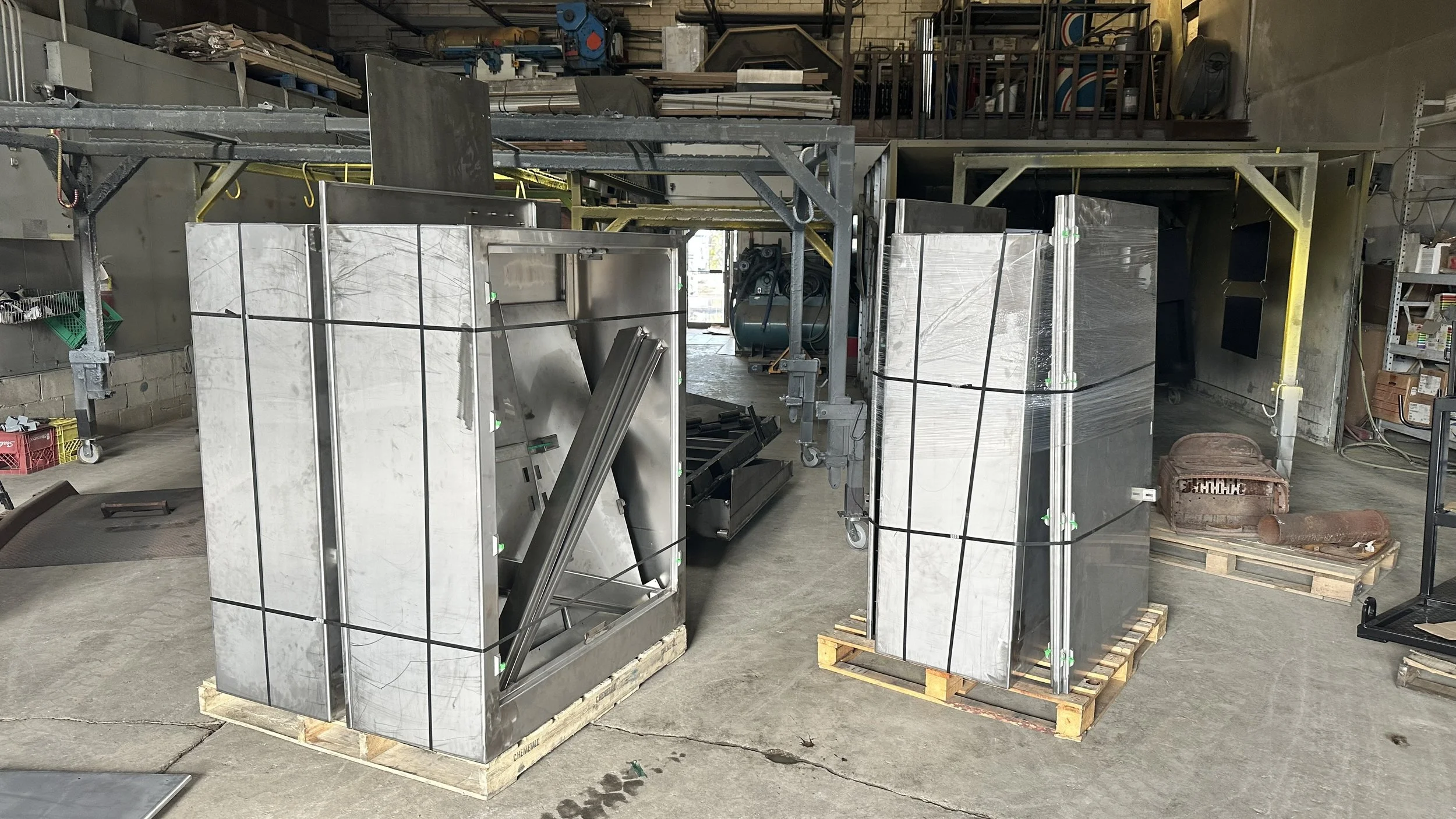 Metal construction materials and equipment stored on wooden pallets in an industrial workshop.