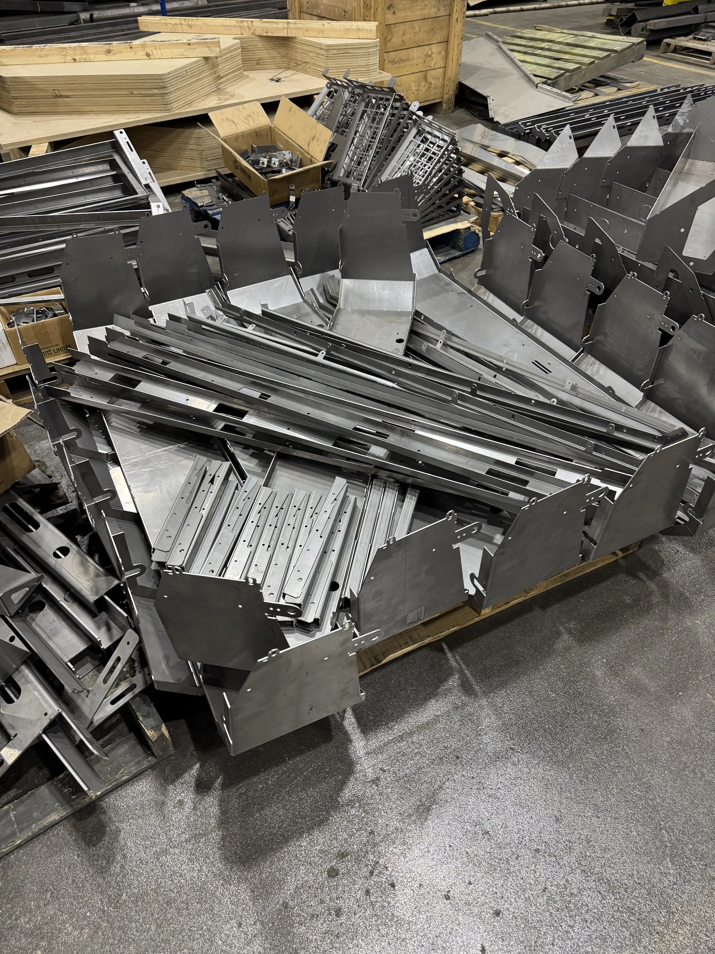 Metal parts and components assembled in a large industrial manufacturing setting, with wooden crates and tools around.