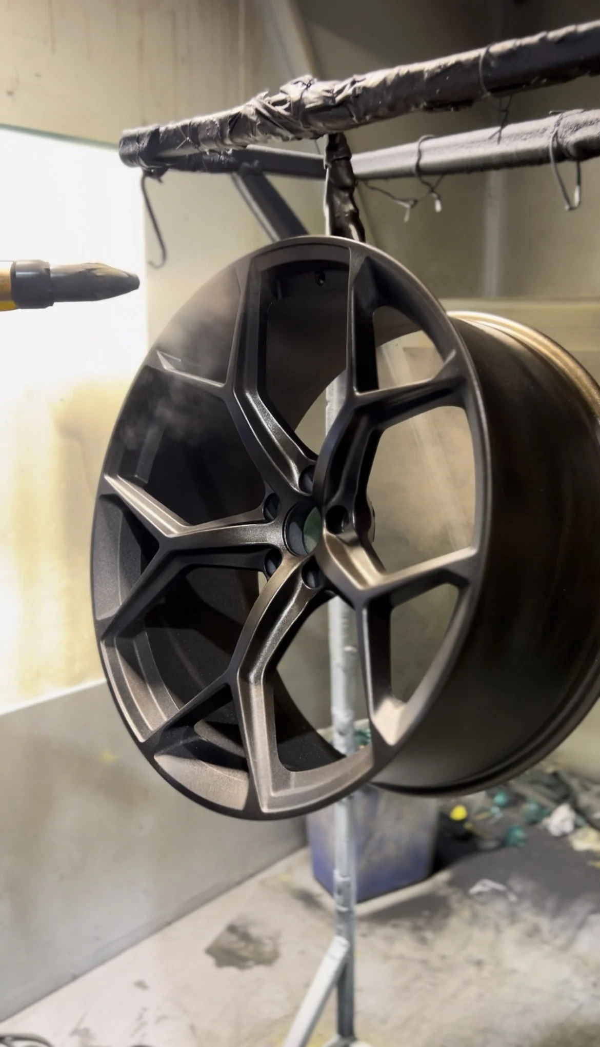 A matte black alloy wheel mounted on a rotating device for painting or coating in a workshop.